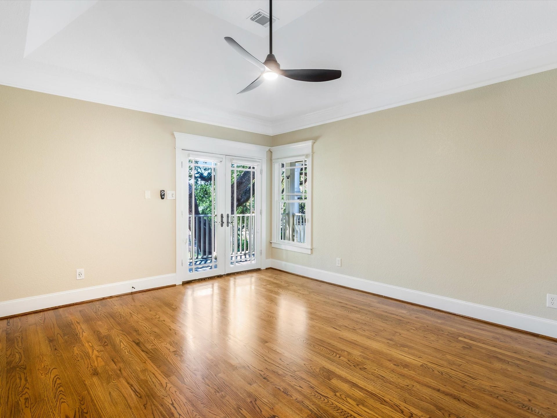 837 E 27th Street, Houston, TX 77009 Spacious primary suite with elegant hardwood floors, a modern ceiling fan, and French doors leading to a charming outdoor view.