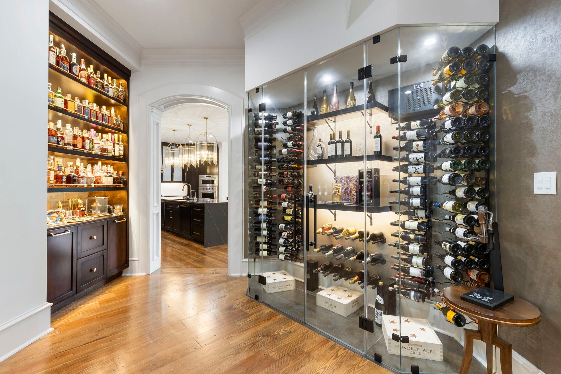 Temperature-controlled glass wine wall with full-height bottle racking sits opposite a butler's bar with illuminated open shelving, creating a true collector's showcase steps from the kitchen and formal entertaining spaces.