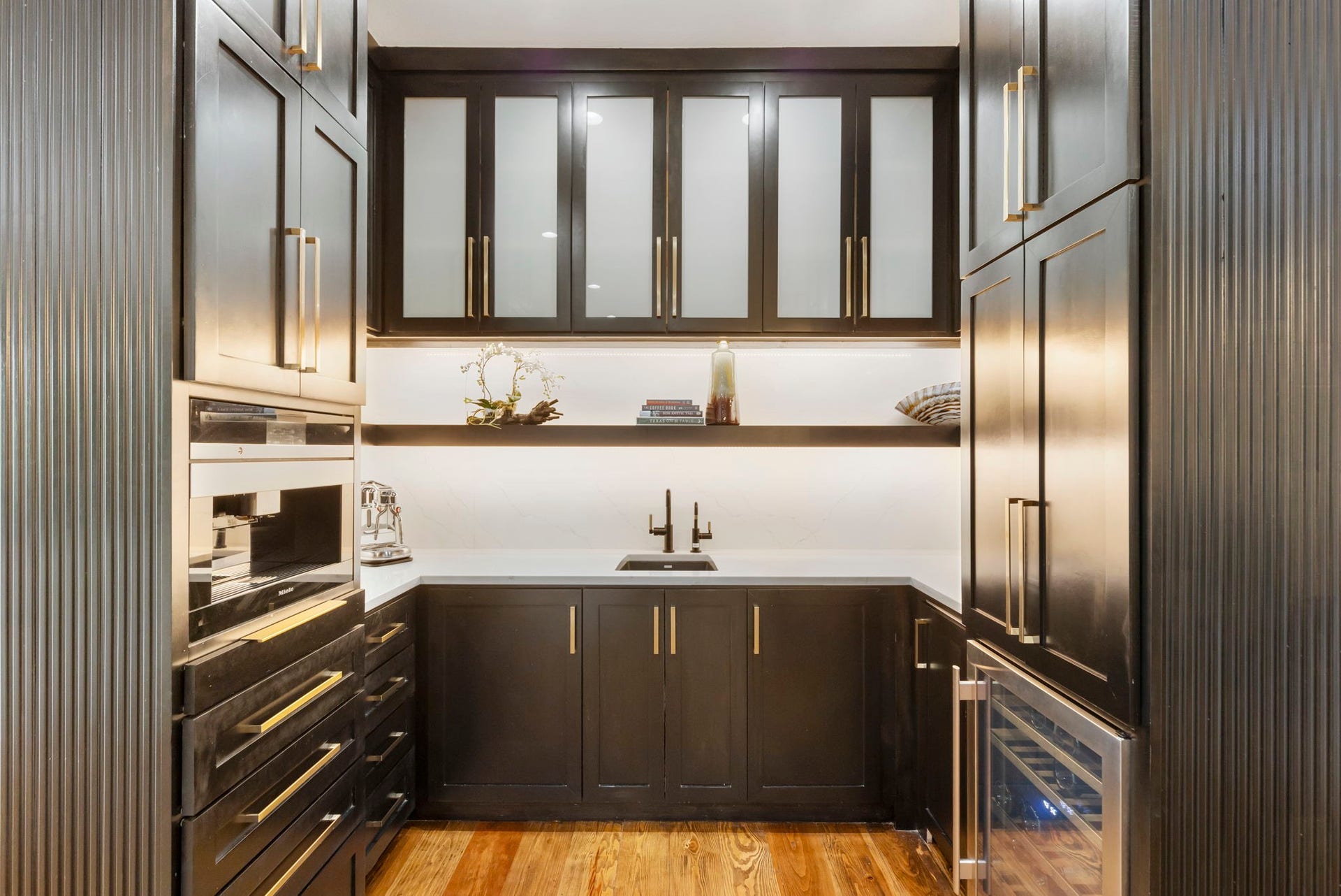 Espresso custom cabinetry with long brass pulls & frosted-glass uppers line the coffee bar complete with Miele coffee/espresso maker and beverage fridge.