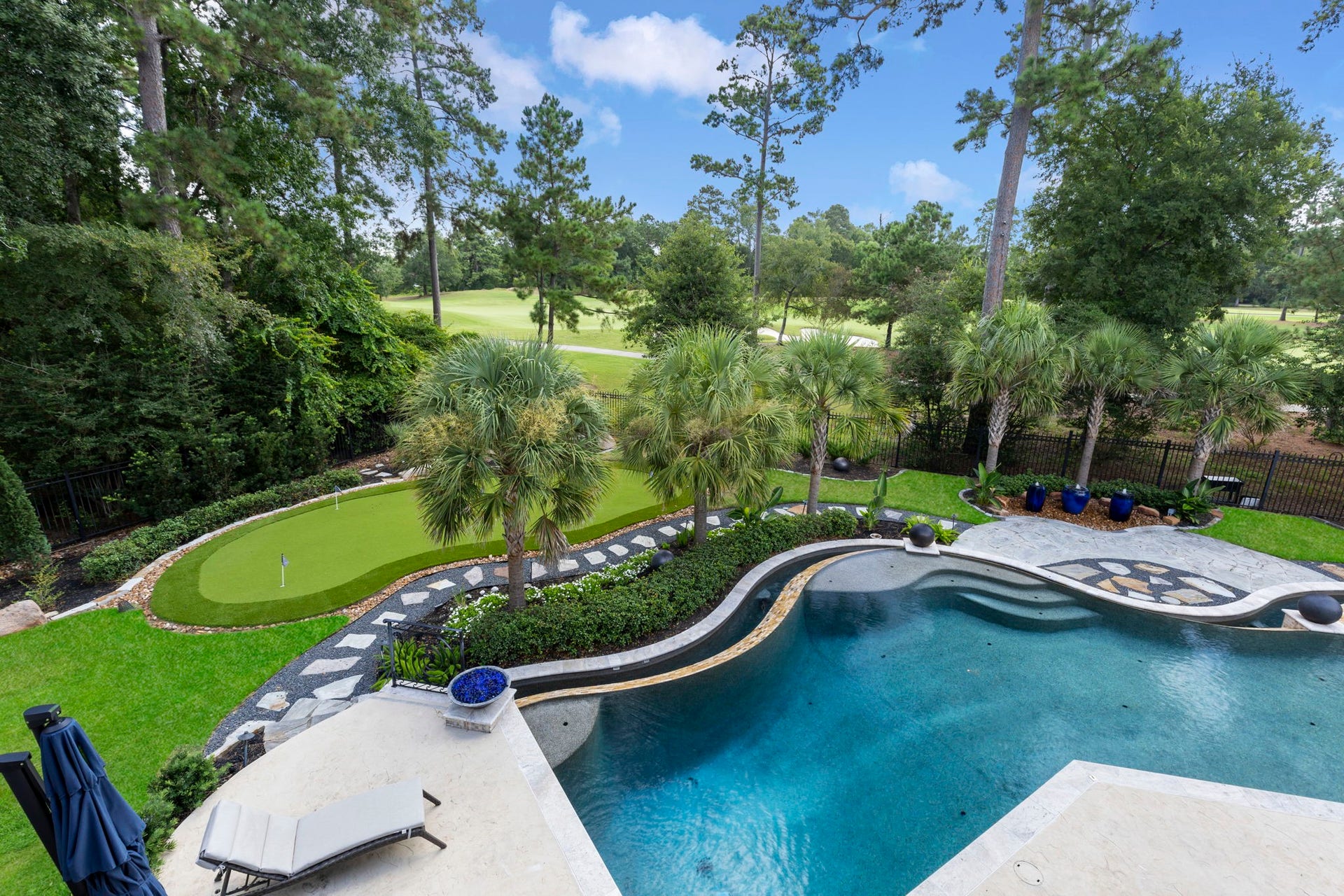 The redesigned backyard centers on a resort-style pool framed by mature palms & a private putting green. Fire bowls & urn water features dot the travertine surround, while a stone walkway winds past the putting green.