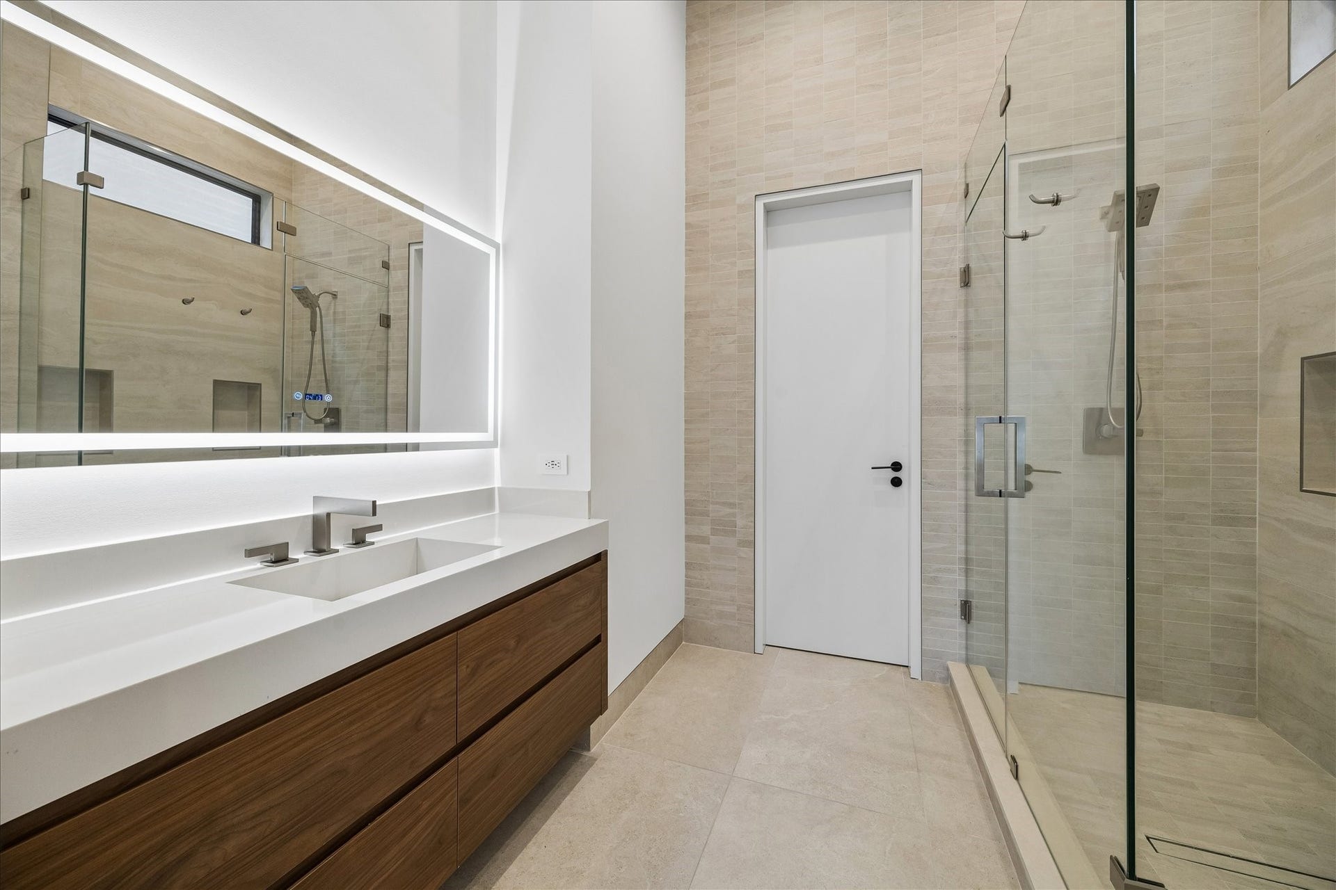 Full bathroom off the guest suite includes a closet and offers sleek design featuring a large, LED illuminated mirror. Spacious glass-enclosed shower finished with neutral-toned tiles for a clean, elegant look.