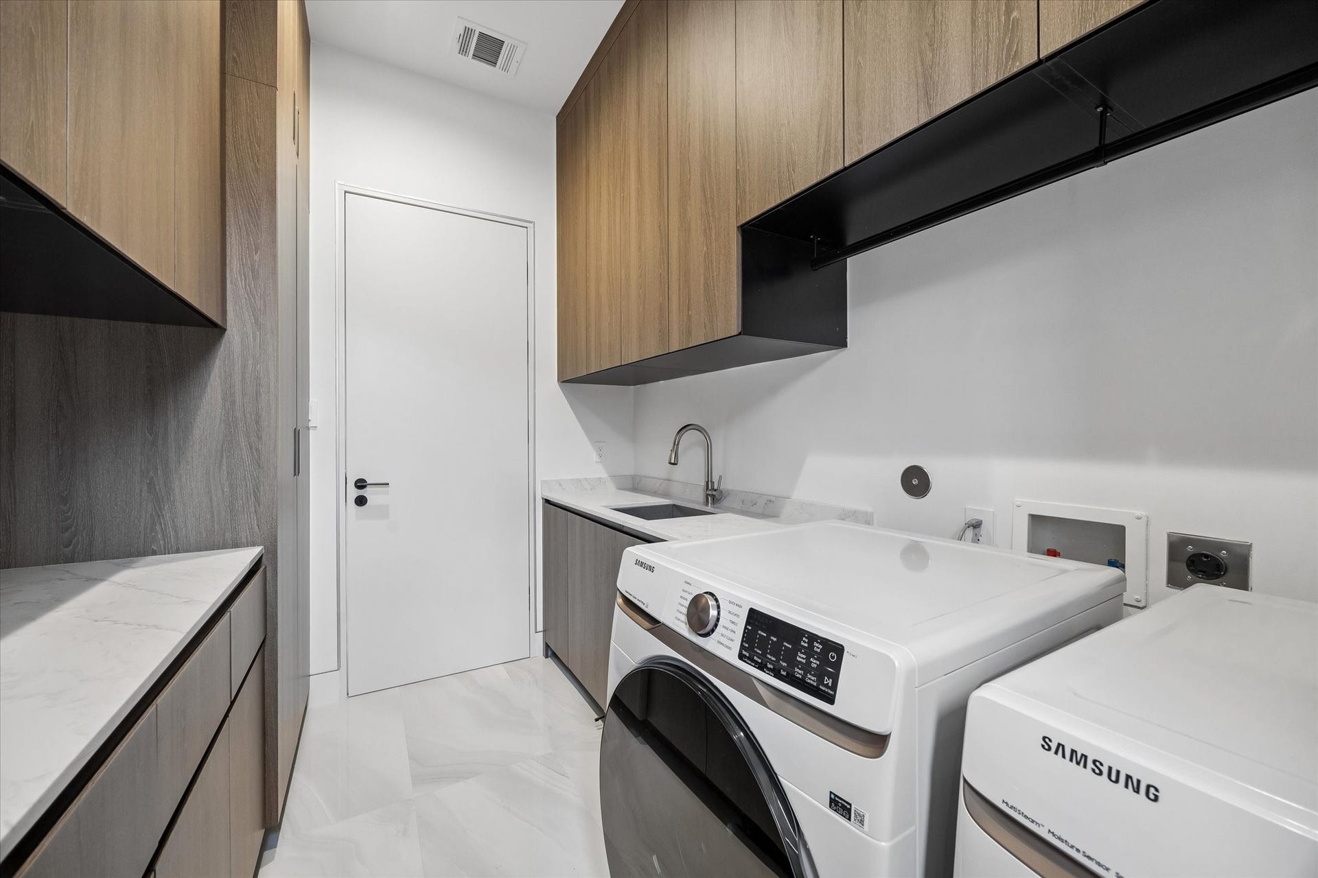 The laundry room features a sink along with sleek cabinetry offering abundant storage
