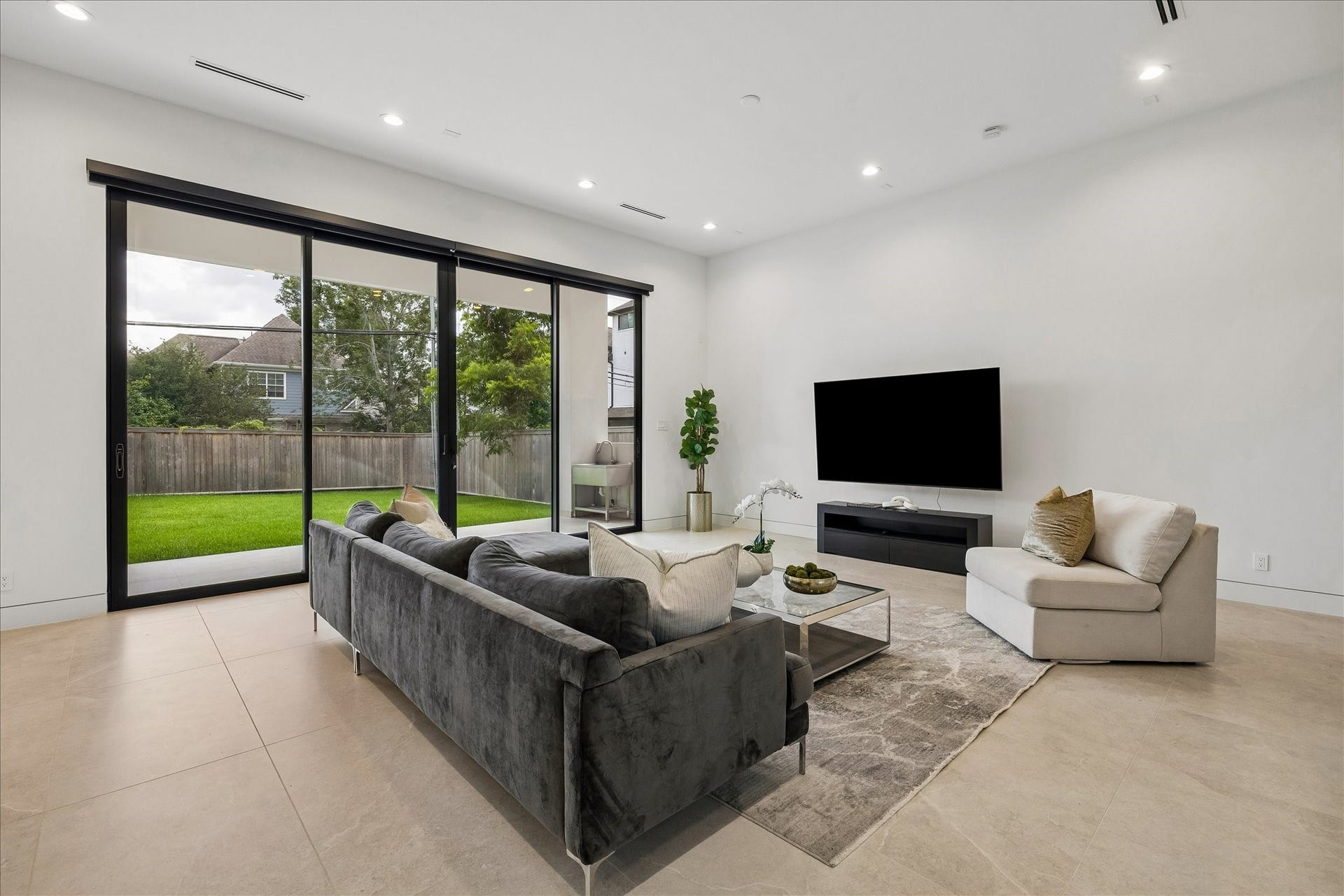 The spacious living room features a modern design with large sliding glass doors that offer abundant natural light and a view of the backyard. An inviting space for relaxation and entertainment.