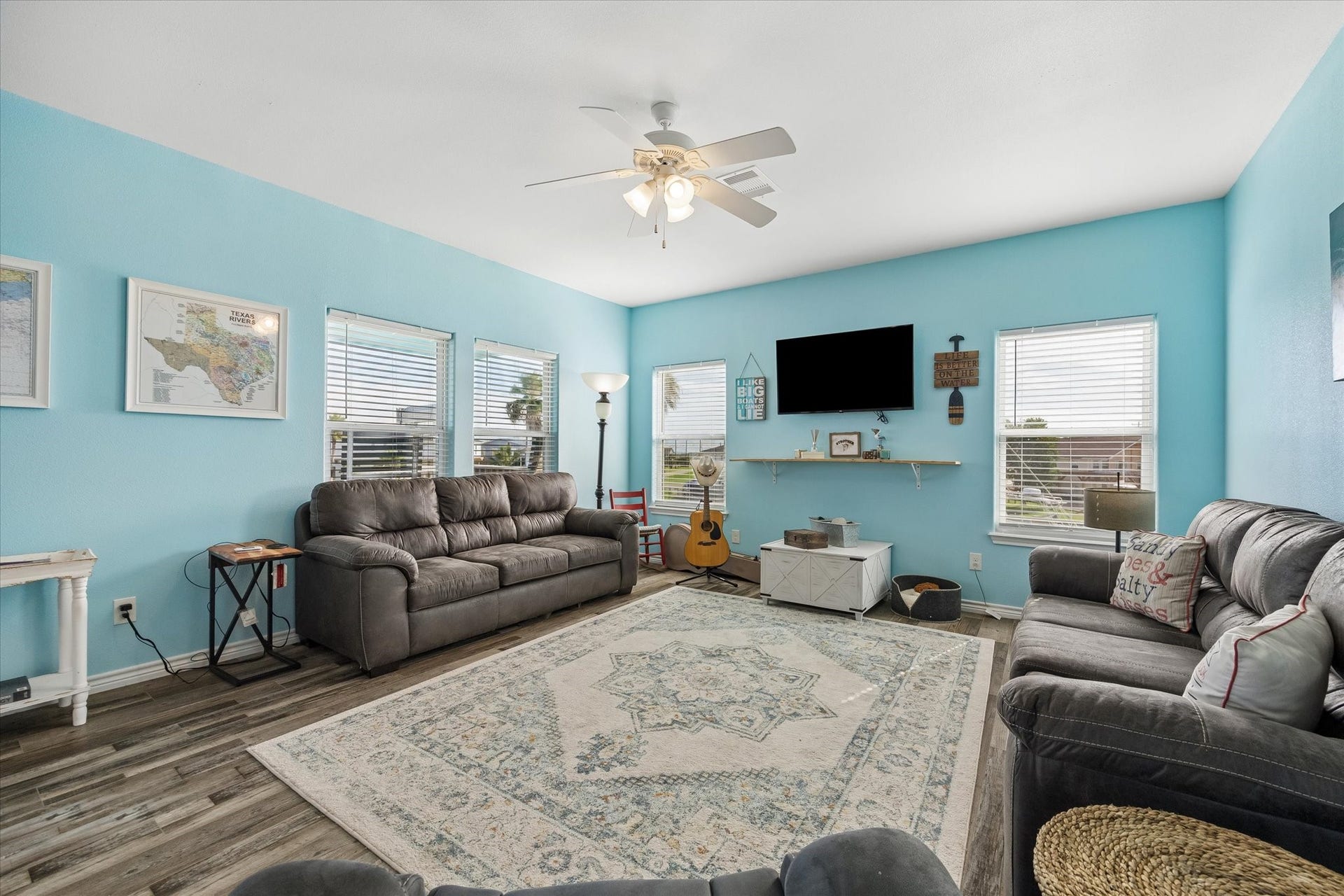 161 Four Master Road, Freeport, TX 77541 Bright and inviting living room with soft blue walls, ample natural light from multiple windows and a ceiling fan for comfort.