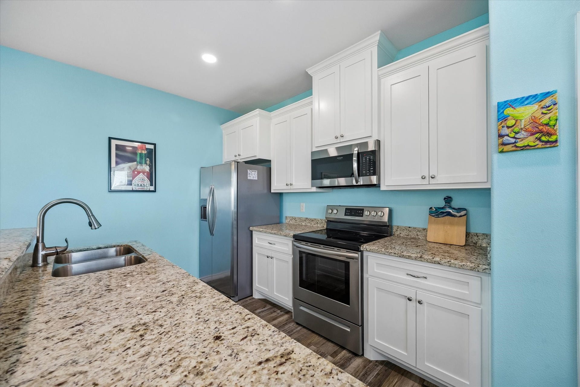 161 Four Master Road, Freeport, TX 77541 A bright and inviting kitchen features granite countertops, stainless steel appliances, and crisp white cabinetry set against a cheerful blue backdrop.