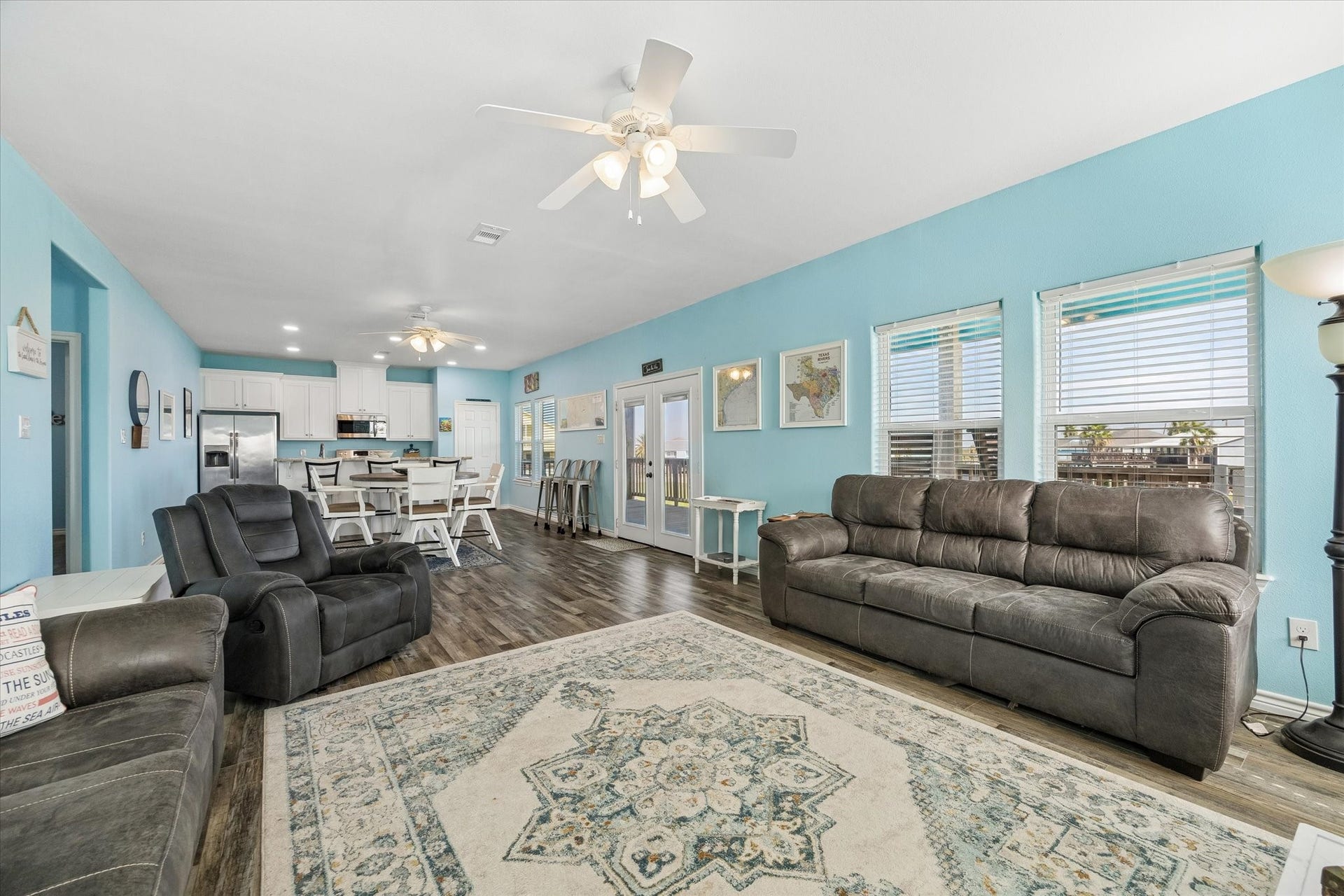 161 Four Master Road, Freeport, TX 77541 Spacious open-concept living area with vibrant blue walls, modern ceiling fans, and ample natural light. The room features seamless flow into a contemporary kitchen with sleek white cabinetry and a breakfast bar.