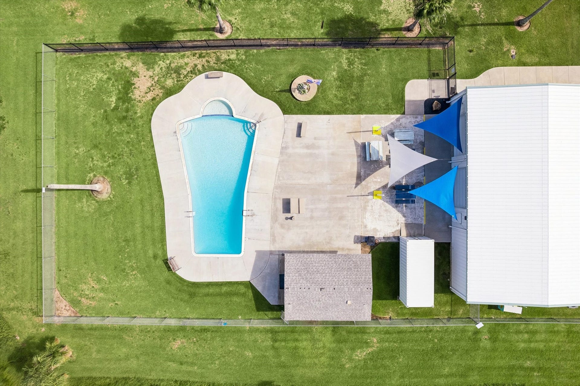 161 Four Master Road, Freeport, TX 77541 Spacious Nieborhood oasis featuring a sparkling pool, expansive patio with shade sails, and lush green lawn, perfect for outdoor entertaining and relaxation.