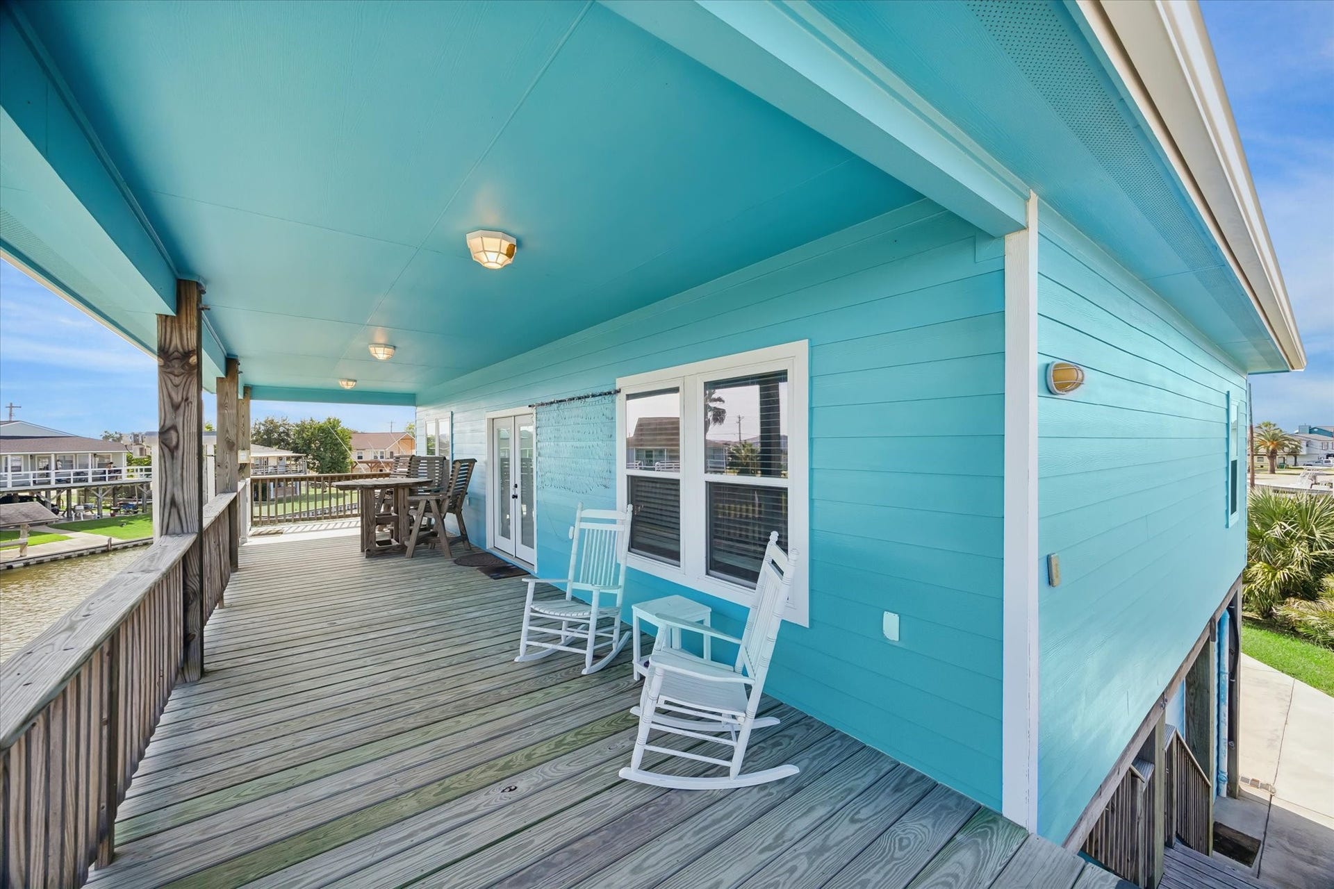 161 Four Master Road, Freeport, TX 77541 Charming coastal retreat with vibrant turquoise siding and a spacious wooden deck, perfect for relaxing in rocking chairs and enjoying outdoor dining.