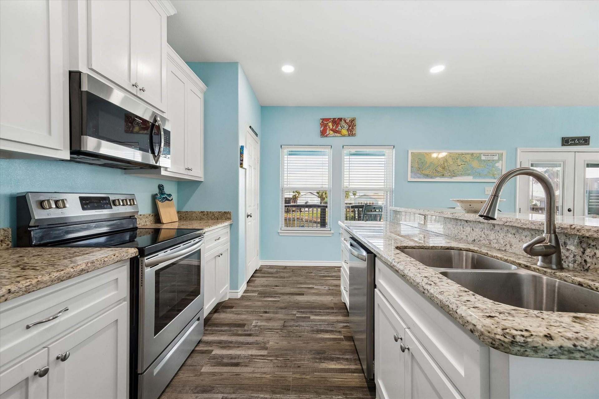 161 Four Master Road, Freeport, TX 77541 Bright and inviting kitchen featuring granite countertops, stainless steel appliances, and charming wood-look flooring, all complemented by soothing blue walls and ample natural light.