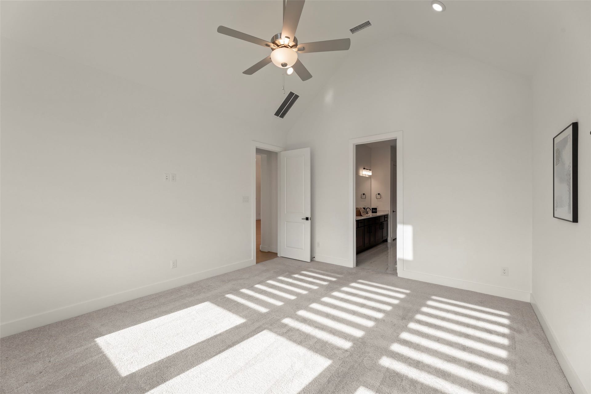 2015 Jade Manor Drive, Rosenberg, TX 77469 Sunlit bedroom with a vaulted ceiling, modern ceiling fan, and plush carpeting, leading to a sleek ensuite bathroom.