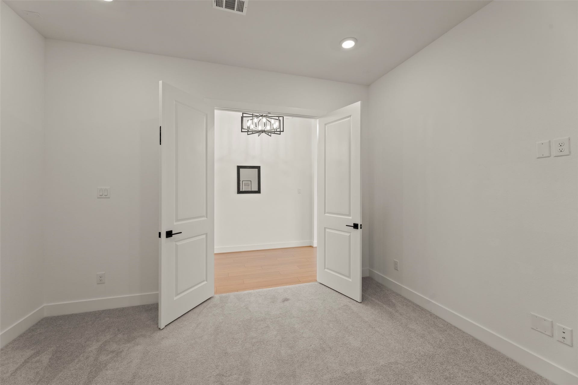 2015 Jade Manor Drive, Rosenberg, TX 77469 Bright room featuring plush carpeting and modern double doors leading to a hardwood-floored area, highlighted by a stylish light fixture.
