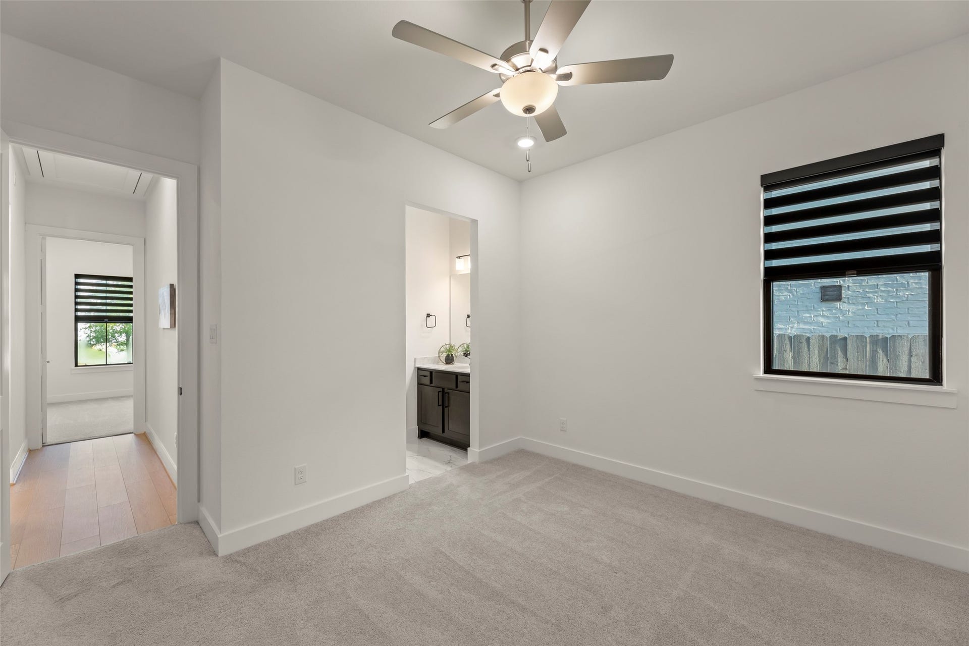 2015 Jade Manor Drive, Rosenberg, TX 77469 Welcoming bedroom featuring plush carpeting, a ceiling fan, and a window with modern blinds. The room connects to a hallway and an adjoining bathroom with sleek fixtures.