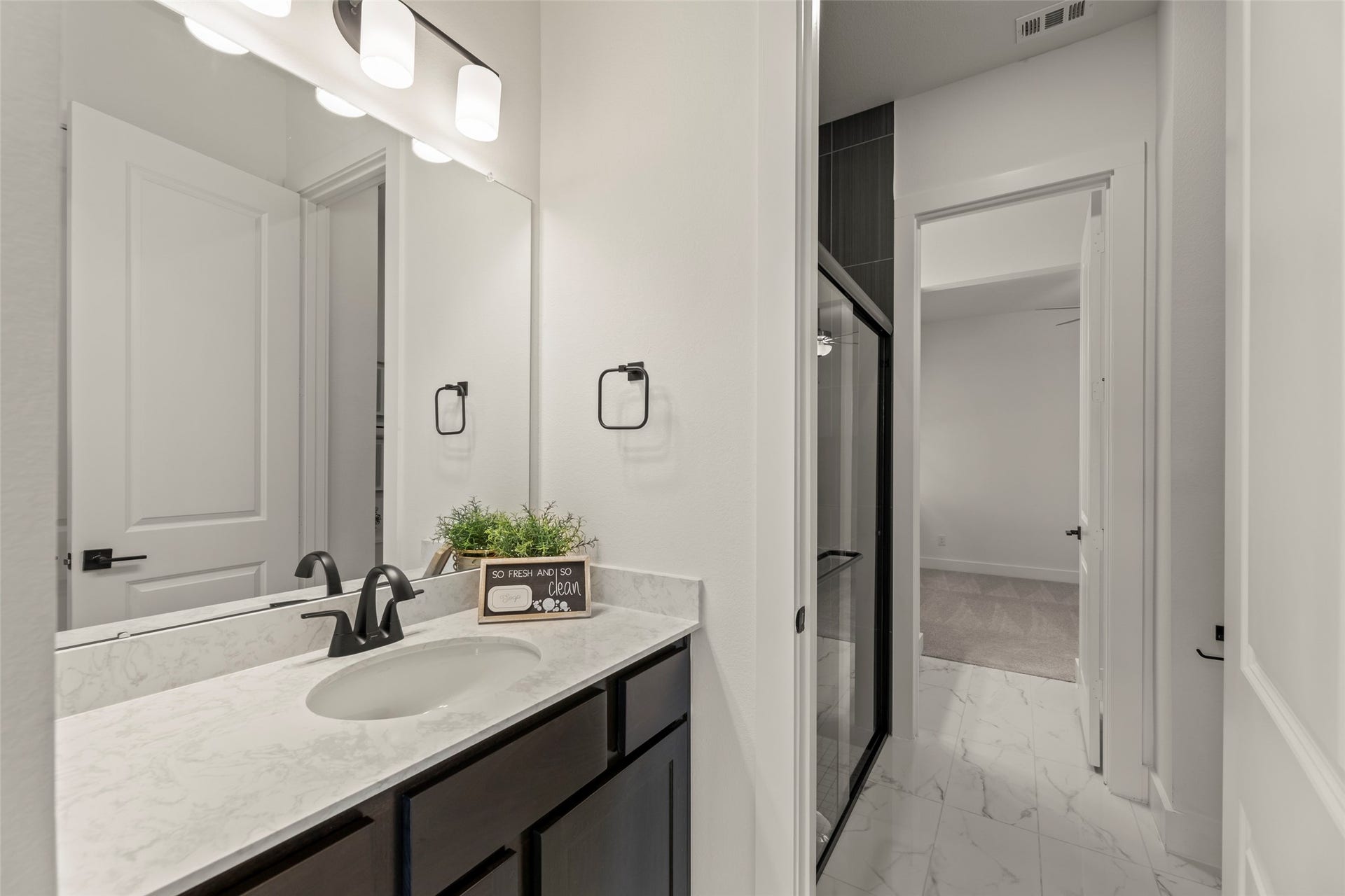 2015 Jade Manor Drive, Rosenberg, TX 77469 Lovely bathroom featuring a modern vanity with a sleek marble countertop and dark cabinetry, complemented by contemporary lighting and a spacious shower with glass doors.
