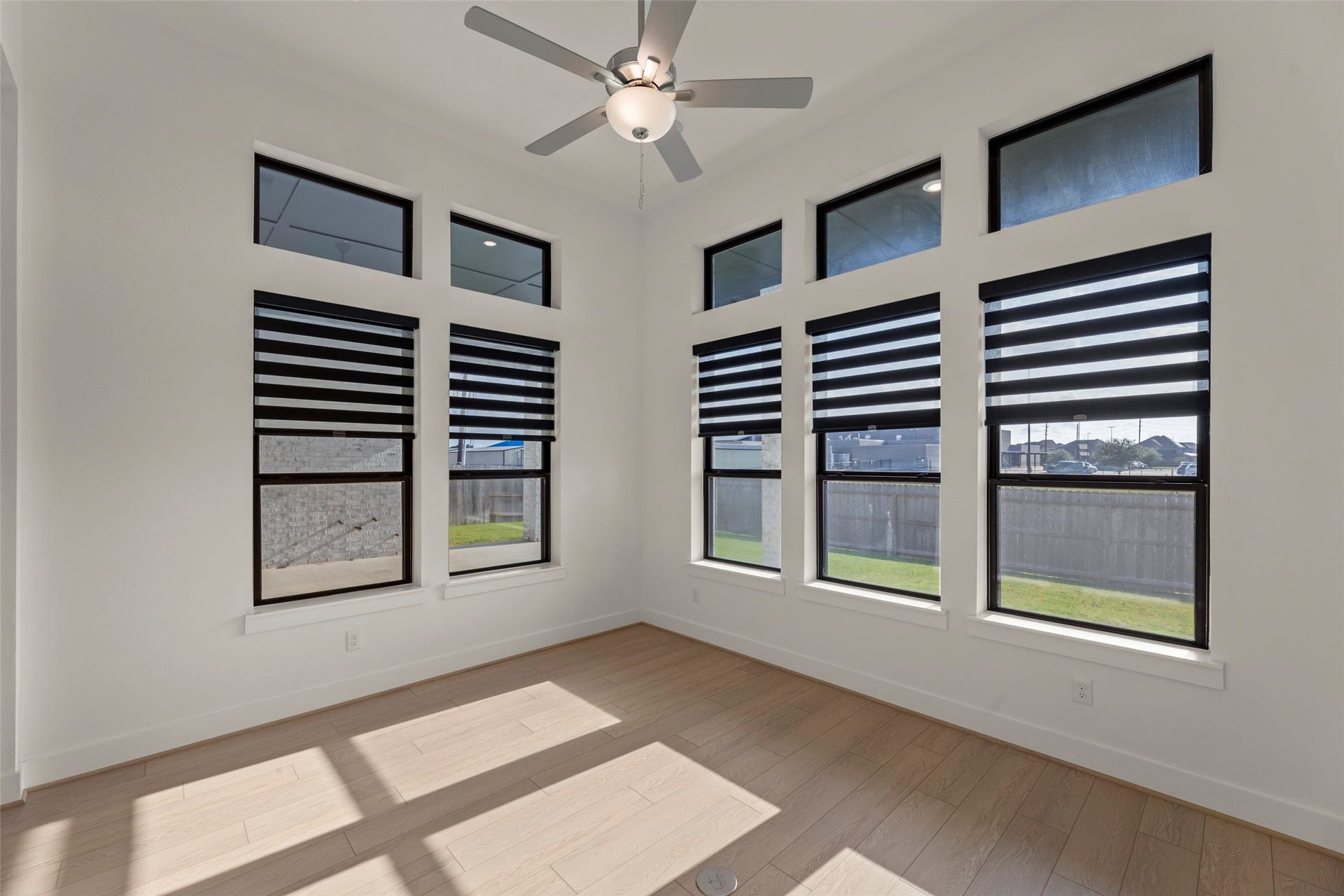 2015 Jade Manor Drive, Rosenberg, TX 77469 Airy room featuring large windows with modern blinds, light wood flooring, and a ceiling fan, perfect for relaxation or a home office setup.