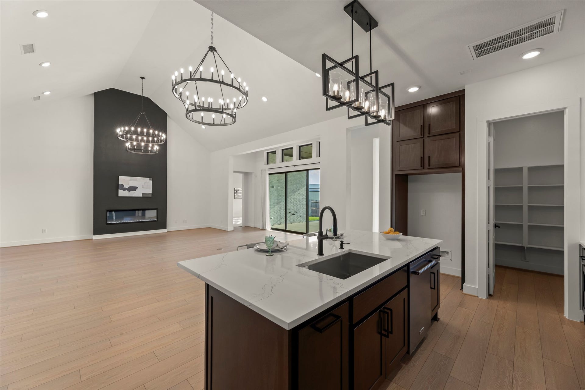 2015 Jade Manor Drive, Rosenberg, TX 77469 High ceilings, modern chandeliers, and a sleek fireplace. The kitchen features a large island with a marble countertop and ample storage space, seamlessly connecting to the living space.