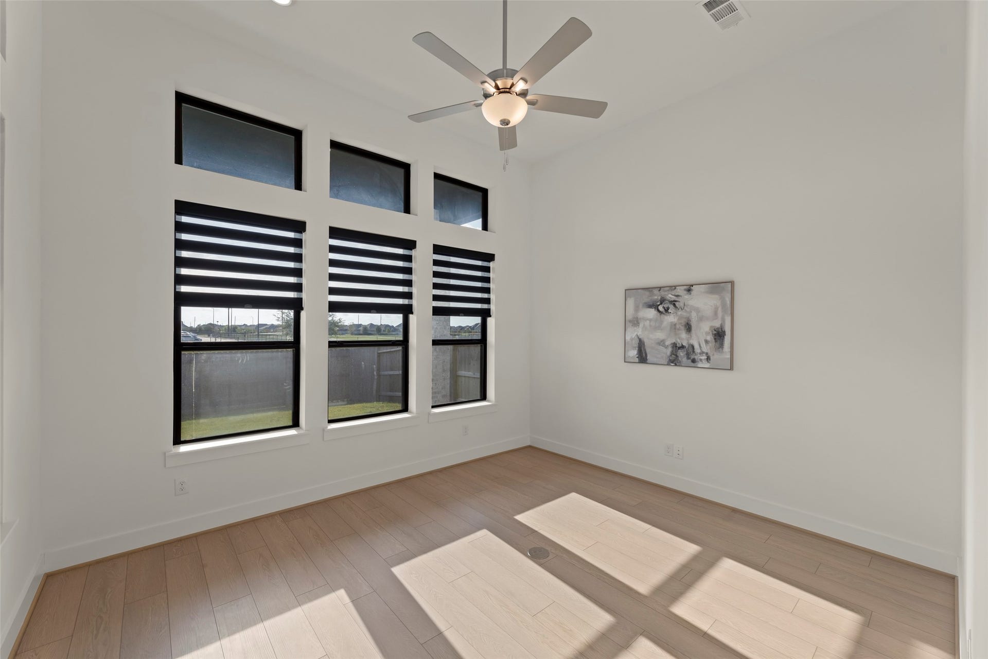 2015 Jade Manor Drive, Rosenberg, TX 77469 Inviting room featuring large windows with modern blinds, sleek ceiling fan, and light wood flooring, perfect for a tranquil retreat.