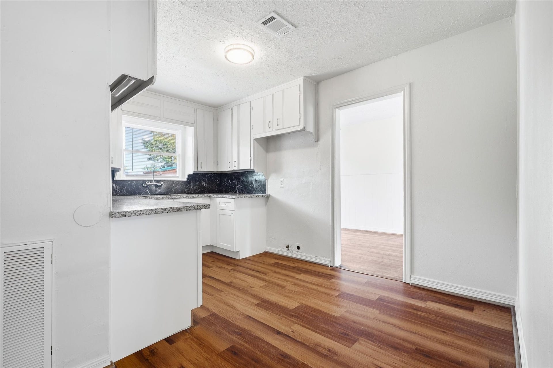 6630 Maybank Drive, Houston, TX 77055 Charming kitchen with rich hardwood floors, sleek granite countertops, and ample white cabinetry, leading into a bright adjoining room.