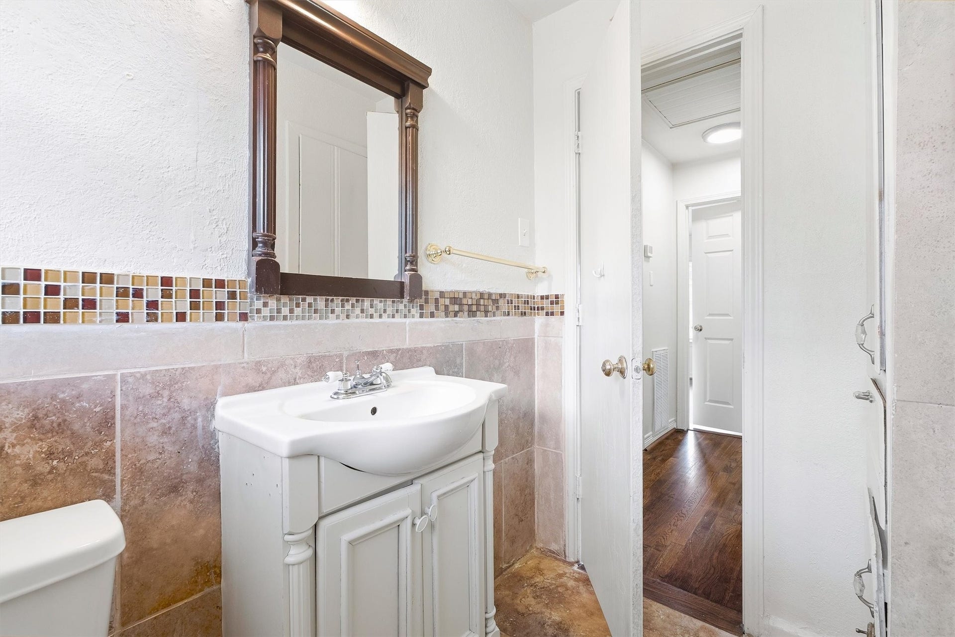6630 Maybank Drive, Houston, TX 77055 Nice bathroom featuring a classic vanity with a decorative mirror, tile backsplash, and warm-toned flooring leading to a bright hallway.