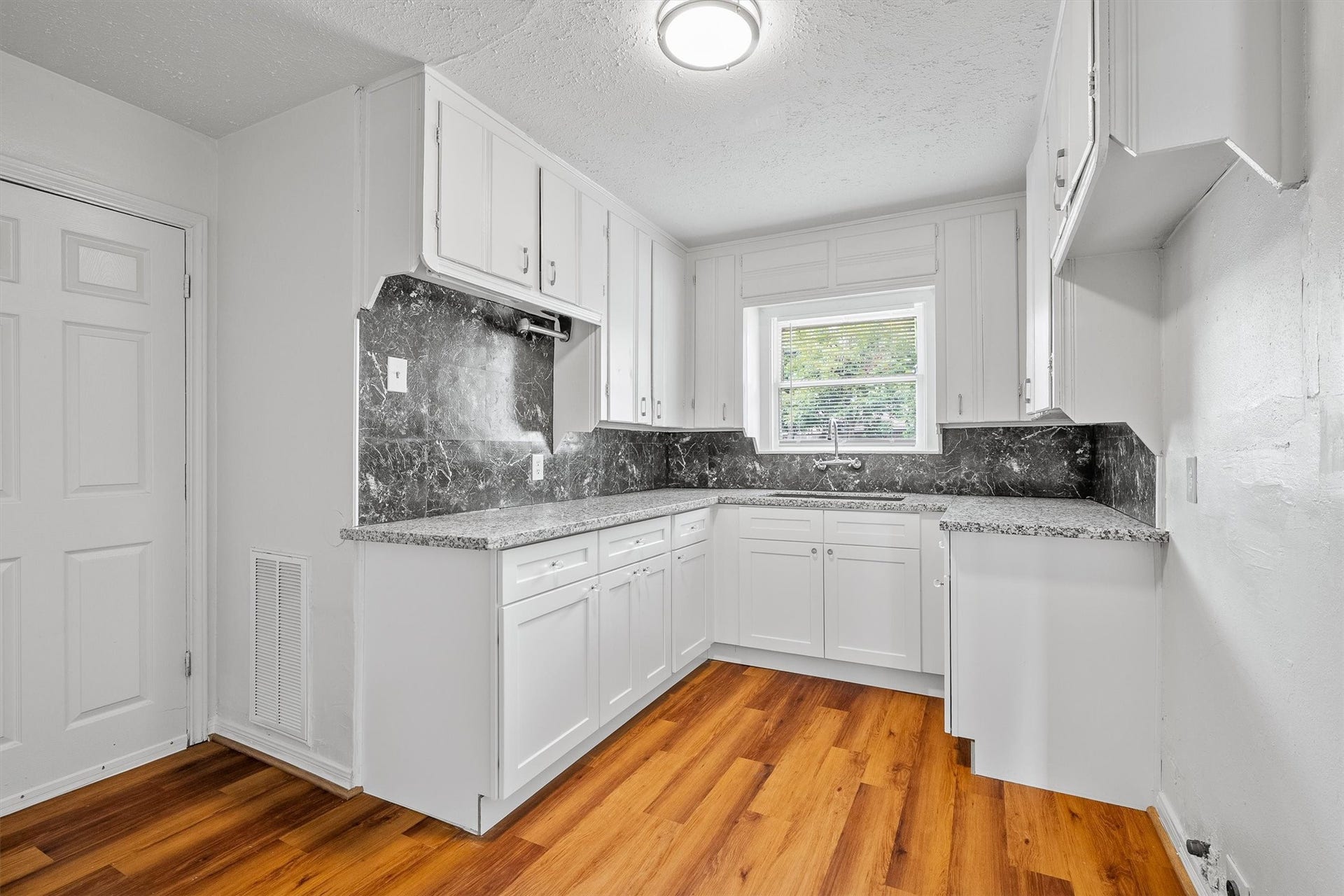 6630 Maybank Drive, Houston, TX 77055 Bright kitchen featuring sleek white cabinetry, elegant dark countertops, and warm wood flooring, offering a charming and functional space.