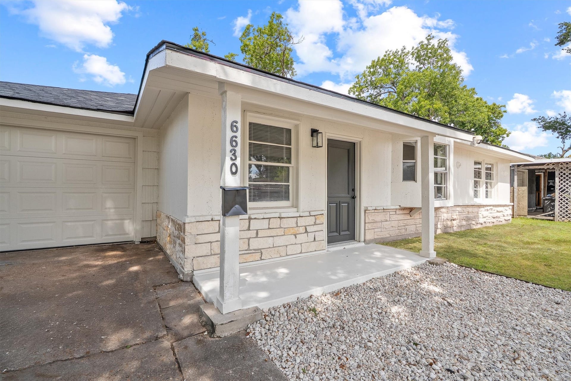 6630 Maybank Drive, Houston, TX 77055 Charming single-story home with a welcoming front porch, stone accents, and a spacious garage, set against a backdrop of lush greenery.