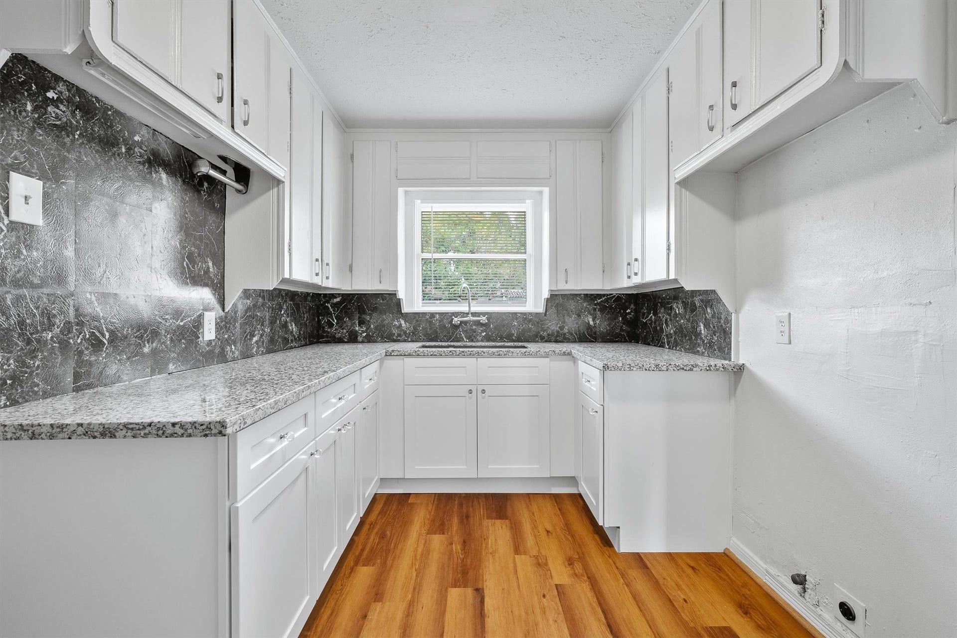 6630 Maybank Drive, Houston, TX 77055 Bright kitchen with sleek granite countertops, classic white cabinetry, and a stylish black marble backsplash, complemented by warm wood flooring.