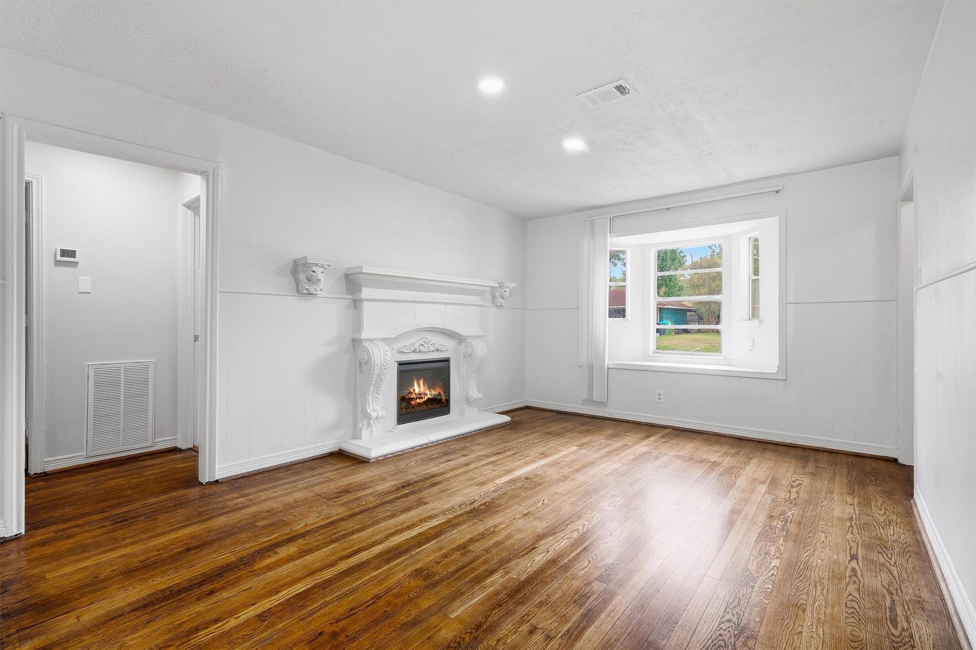 6630 Maybank Drive, Houston, TX 77055 Charming living room with elegant white paneled walls, a decorative fireplace, and beautifully refinished hardwood floors, complemented by a large window that invites ample natural light.