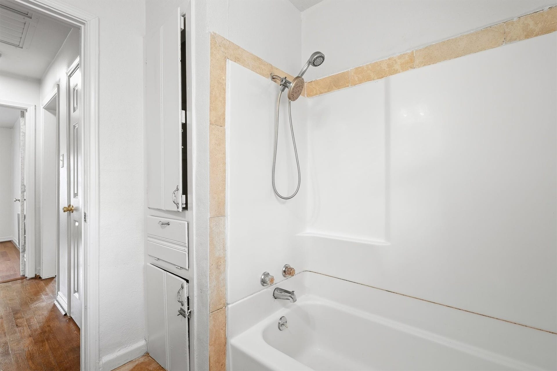 6630 Maybank Drive, Houston, TX 77055 Bright and clean bathroom featuring a classic bathtub with shower, accented by tasteful tiling and convenient built-in storage.