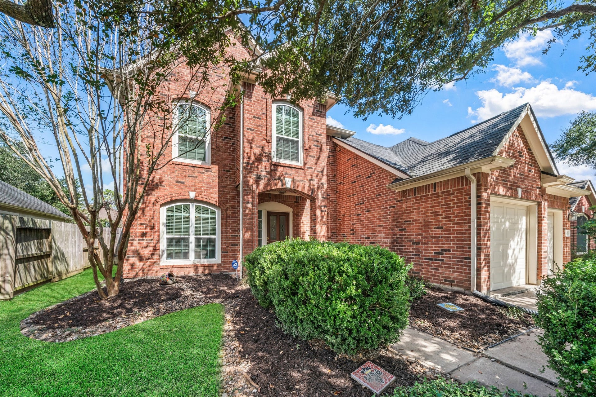 3607 Parkshire Drive, Pearland, TX 77584 Charming two-story brick home with elegant arched windows, lush landscaping, and a welcoming pathway leading to the front entrance.
