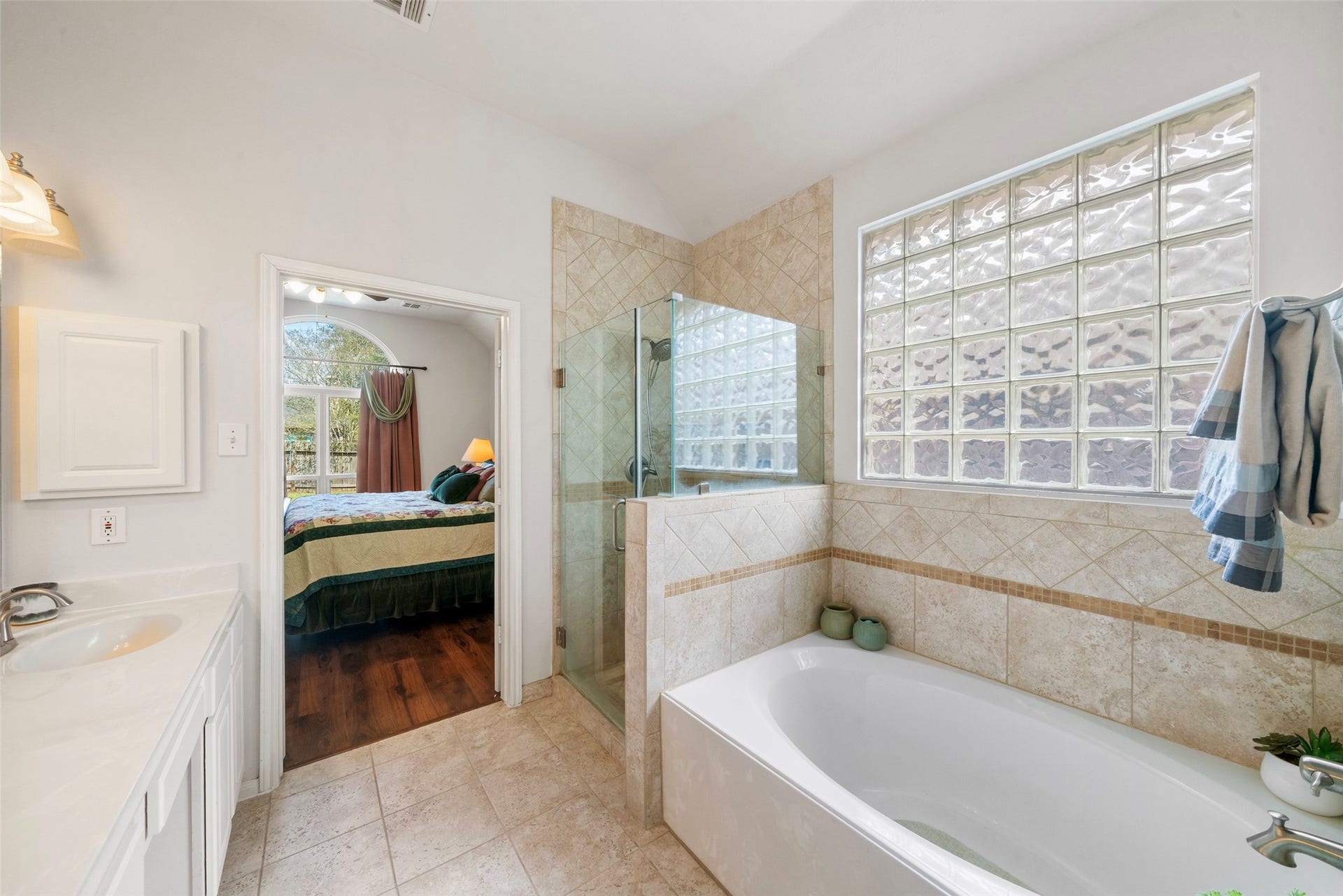 3607 Parkshire Drive, Pearland, TX 77584 Alternate view of updated bathroom featuring a large soaking tub, glass-enclosed shower, and elegant tile work, with plenty of natural light from the glass block windows and an adjoining view into a cozy bedroom.
