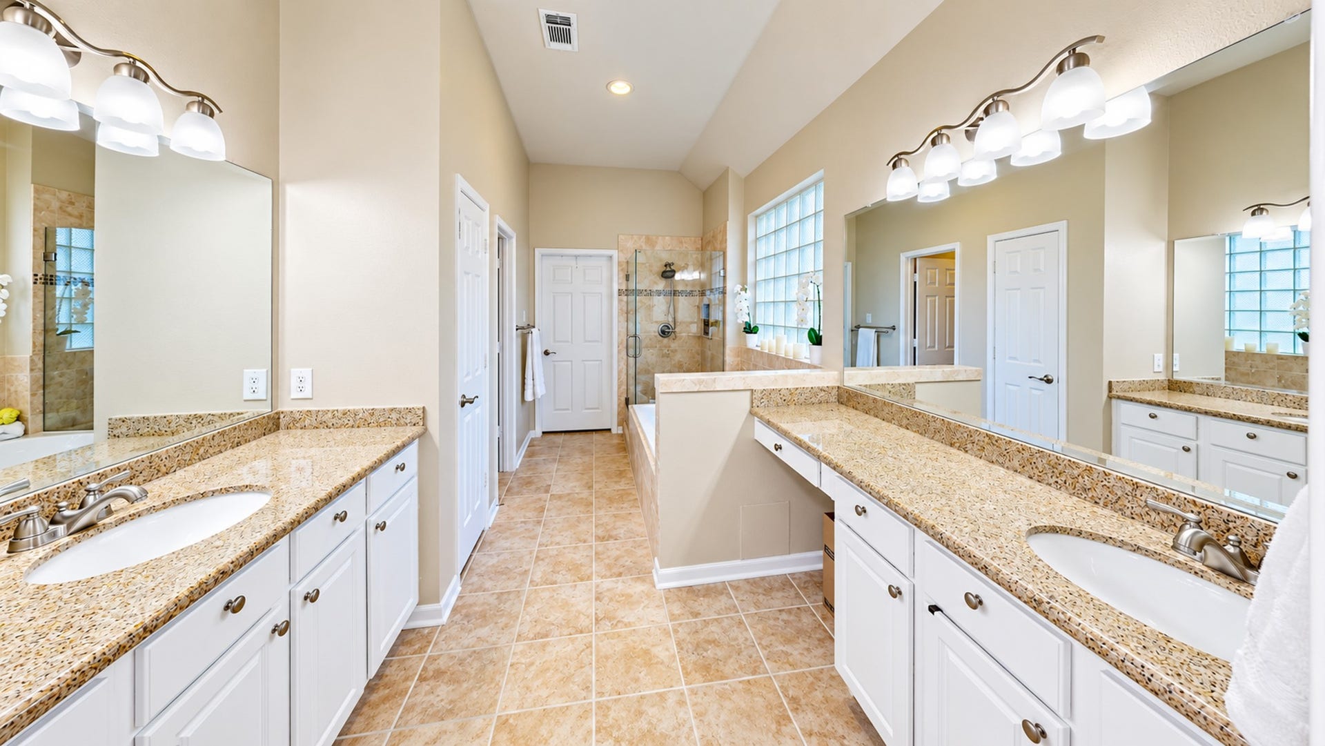 3511 Harbor Pass Lane, Friendswood, TX 77546 Spacious bathroom featuring dual granite-topped vanities, elegant lighting, and a large walk-in shower, all set against warm tile flooring.