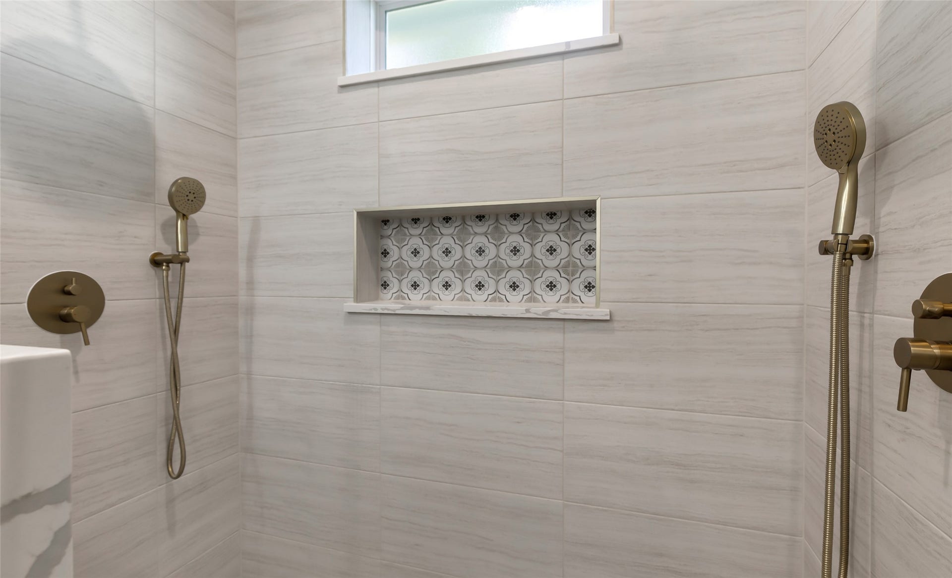 Primary shower, featuring elegant dual showerheads, chic modern tiling, and a stylish recessed shelf for added convenience.