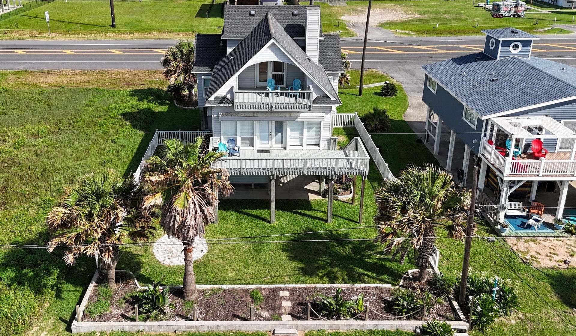 21519 San Luis Pass Road, Galveston, TX 77554 This attractive coastal home features a raised design with a spacious front deck and balcony, perfect for enjoying ocean views. Surrounded by lush greenery and palm trees, it offers a relaxed beachside atmosphere. The house is conveniently located with easy access.