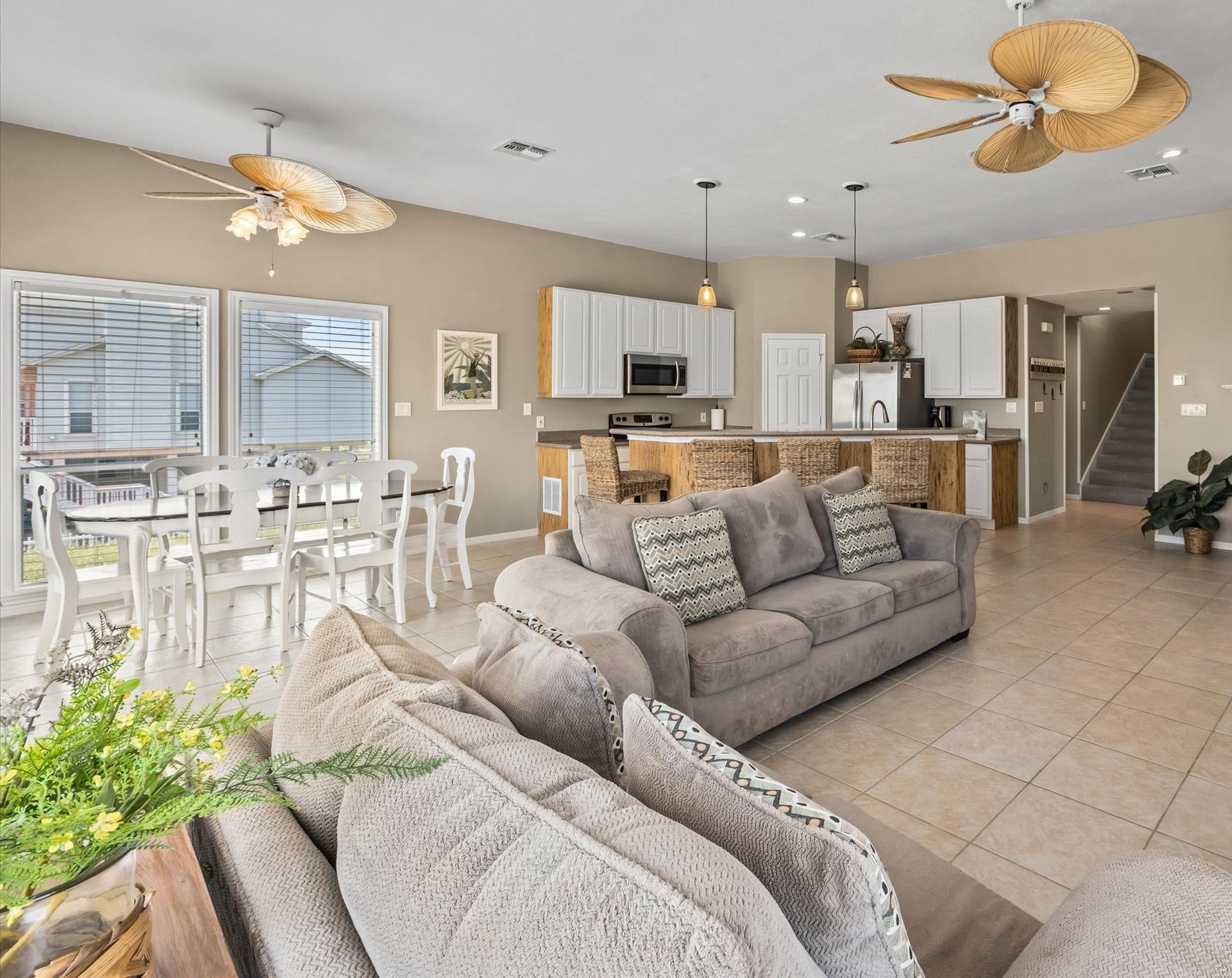 21519 San Luis Pass Road, Galveston, TX 77554 This open-concept living space features a modern kitchen with stainless steel appliances and a breakfast bar, a cozy dining area with natural light, and a comfortable lounge area. The room is adorned with stylish ceiling fans and has a neutral color palette, creating a warm and inviting atmosphere.