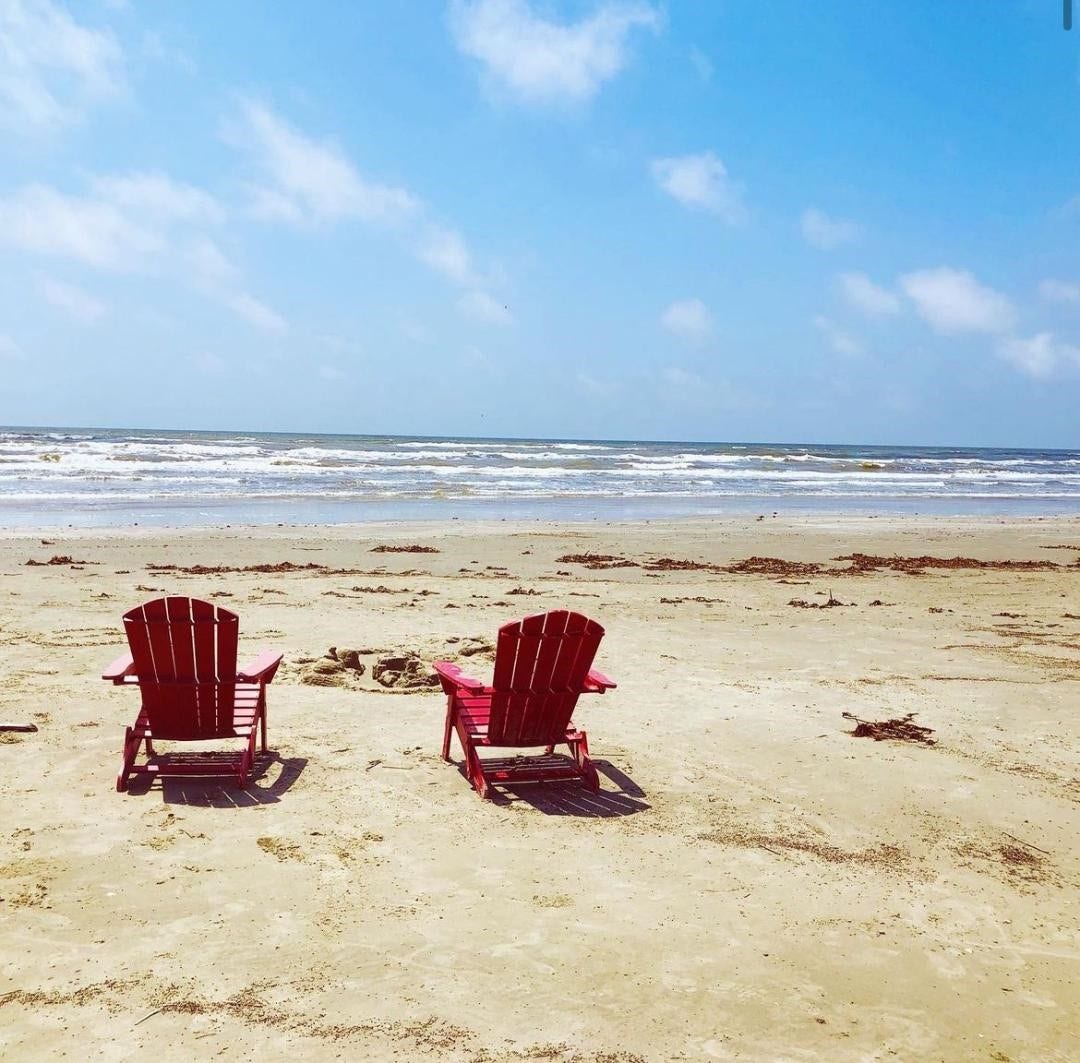 21519 San Luis Pass Road, Galveston, TX 77554 This photo features a serene beach scene with two red Adirondack chairs facing the ocean, perfect for enjoying seaside views and relaxation in a coastal home setting.