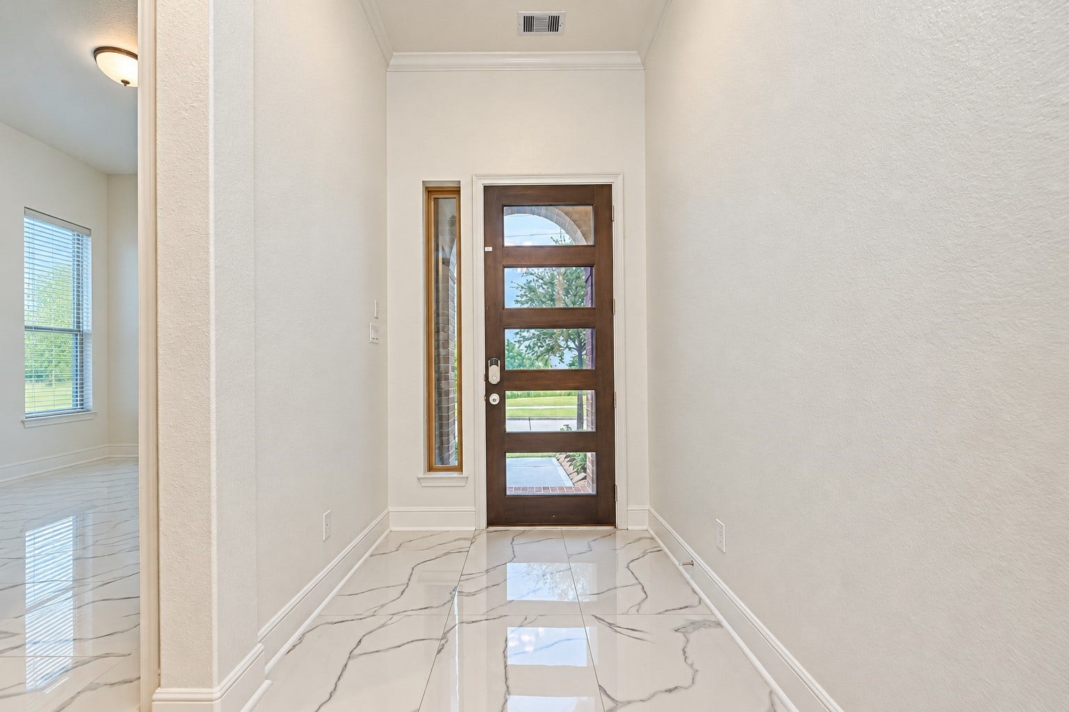 12215 Mackinchan Street, Richmond, TX 77407 A welcoming entryway featuring a striking modern front door with glass panel inserts, elegant marble-like tile flooring, and crisp neutral walls, creating a bright, sophisticated first impression with timeless appeal