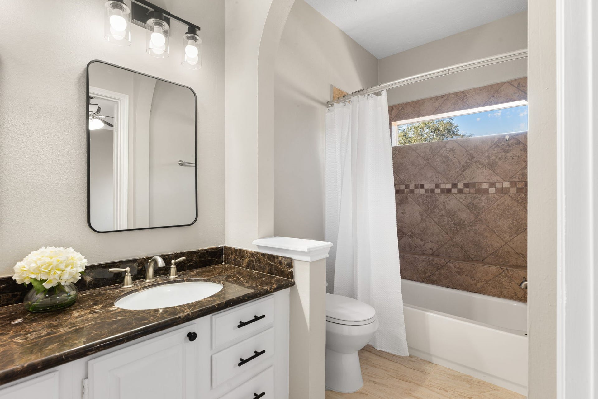 Another view of the primary bath highlights the tub and shower combination, with natural light filtering through the window above.