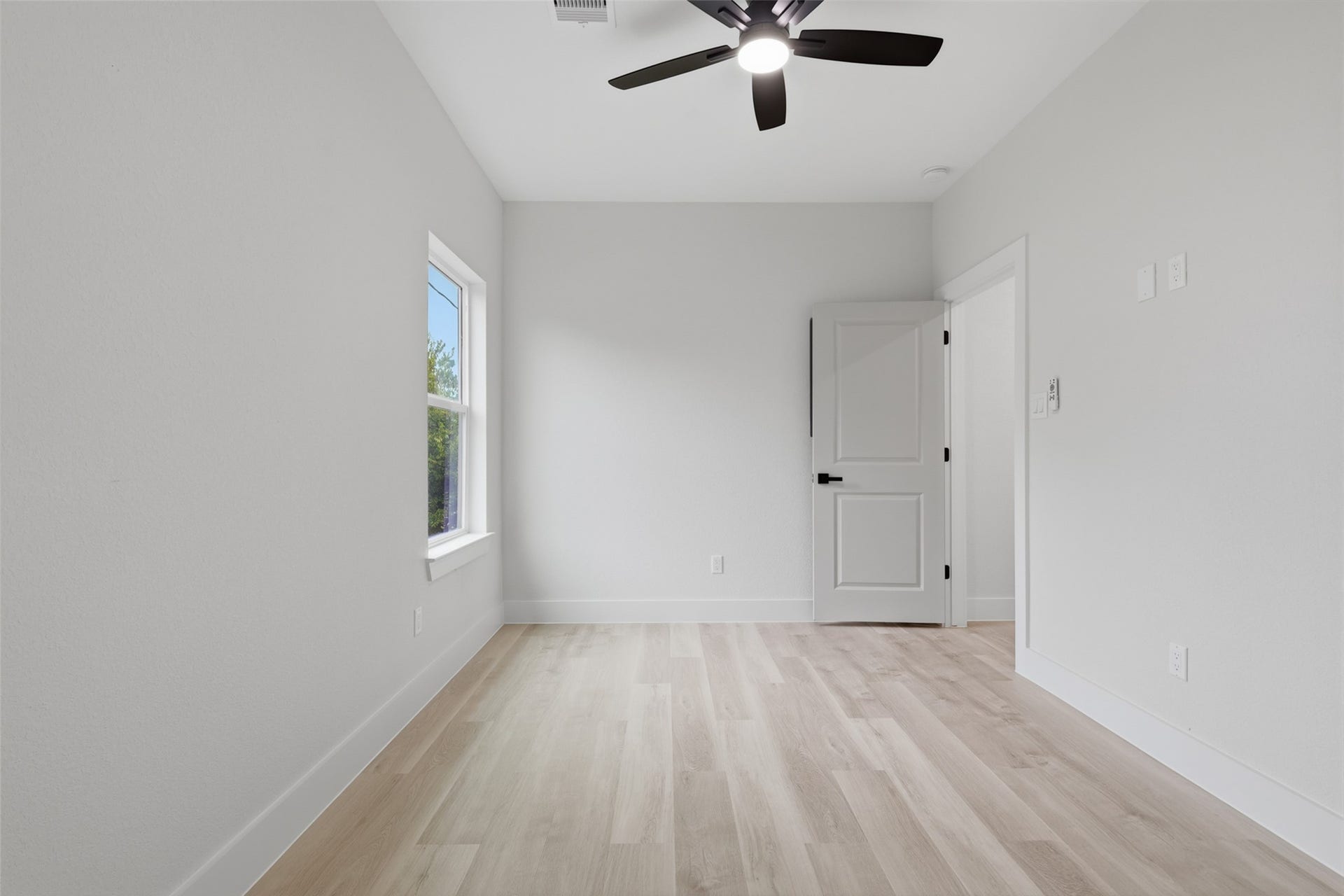 3201 & 3205 Berry Street, #A/B, Houston, TX 77004 Bright and airy room featuring sleek light wood like LVP flooring, a modern ceiling fan, and ample natural light from the window, perfect for a cozy bedroom and an office space for a student or child.