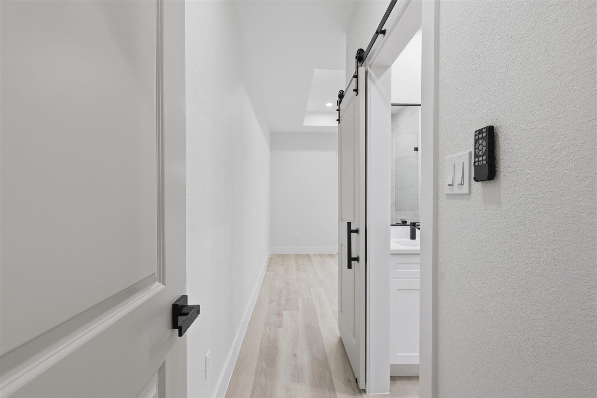 3201 & 3205 Berry Street, #A/B, Houston, TX 77004 Modern hallway with sleek, light wood like flooring for the primary bedroom (upstairs) leading to a space with a stylish sliding barn door to the private bathroom, creating a contemporary and inviting atmosphere.