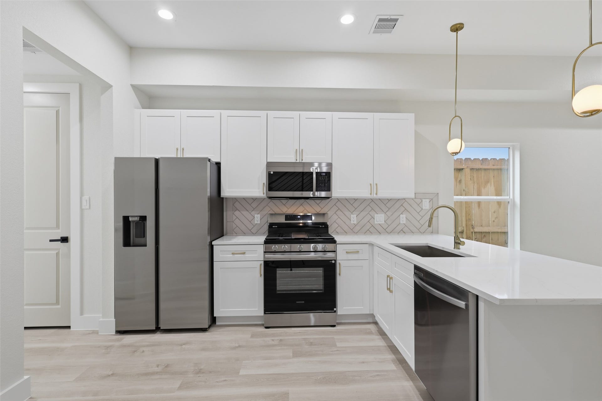 3201 & 3205 Berry Street, #A/B, Houston, TX 77004 Sleek modern kitchen featuring stainless steel appliances, crisp white cabinetry, and a stylish herringbone backsplash, complemented by elegant pendant lighting.
