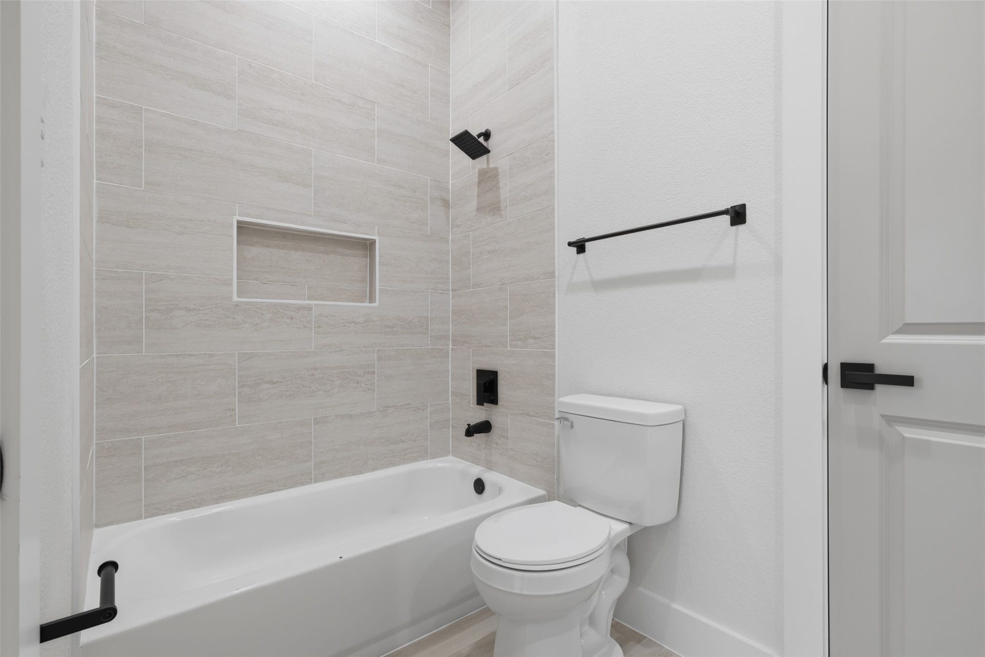 3201 & 3205 Berry Street, #A/B, Houston, TX 77004 Modern bathroom featuring a sleek bathtub with beige tile surround, a convenient built-in shelf, and contemporary black fixtures.