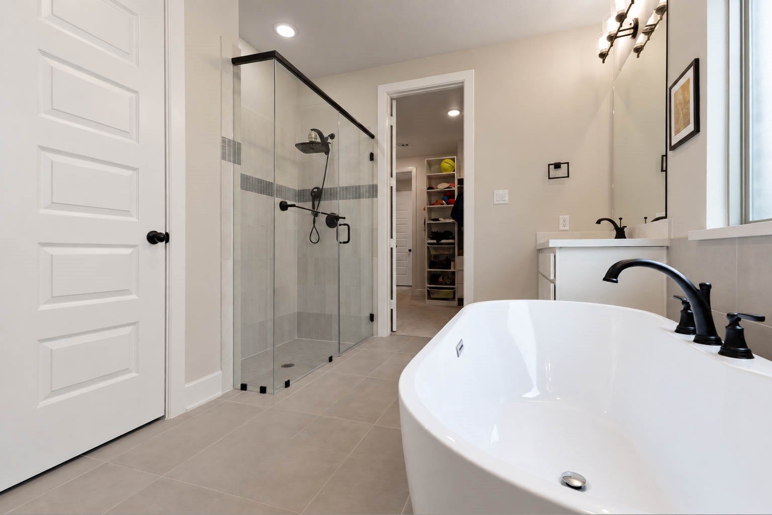 3165 Stingray Cove Drive, Katy, TX 77493 The spa-inspired primary bath continues with an oversized frameless glass-enclosed shower, beautifully finished with a tile surround, rainfall showerhead, & sleek matte black fixtures. A separate water closet provides added privacy, while the expansive walk-in closet offers custom built-ins & direct access to the laundry room.