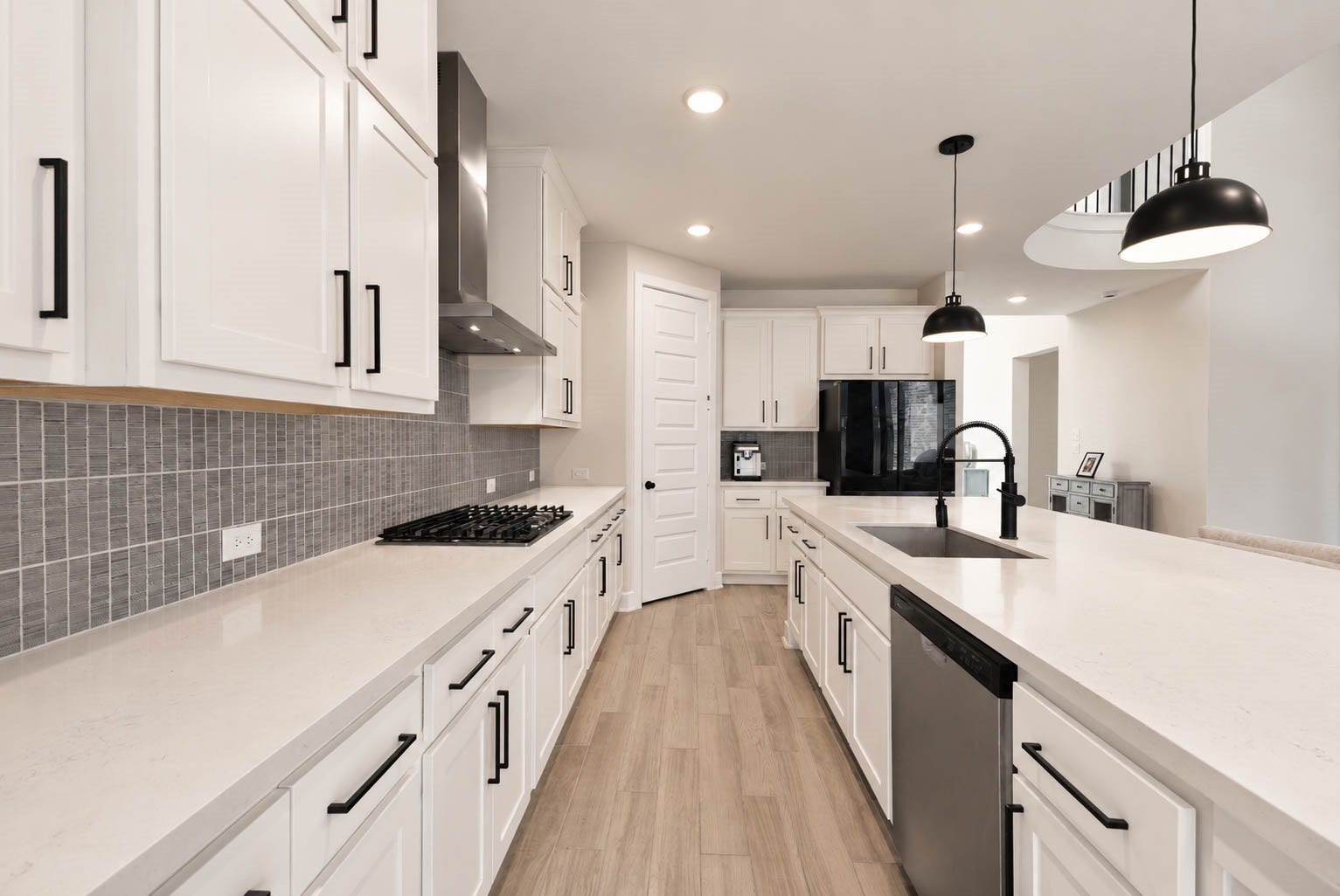 3165 Stingray Cove Drive, Katy, TX 77493 A closer look highlights the kitchens polished finishes, including quartz counters, ample cabinetry, a gray tile backsplash, & matte black hardware. The expansive island offers a farmhouse sink, gooseneck faucet, dishwasher, additional storage, & generous workspace.