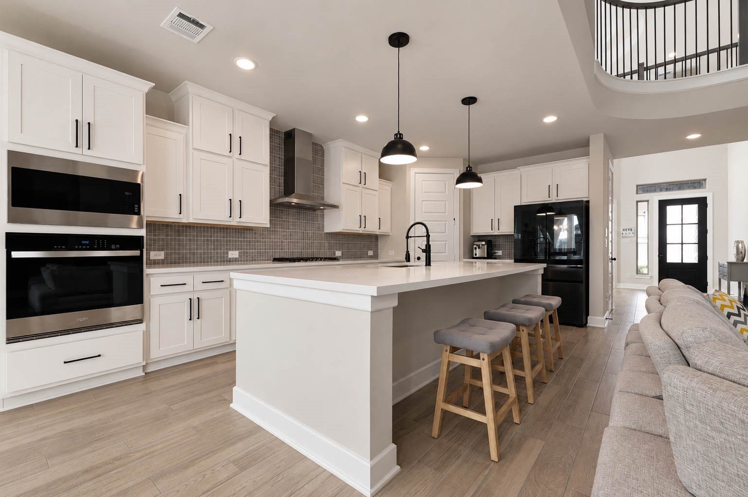 3165 Stingray Cove Drive, Katy, TX 77493 The large center island anchors the space beneath a trio of black pendant lights, while built-in stainless steel appliances, gas cooking, recessed lighting, and extensive counter space combine style with everyday functionality. The open design maintains clear sightlines toward the family room and dramatic upper-level railing beyond.