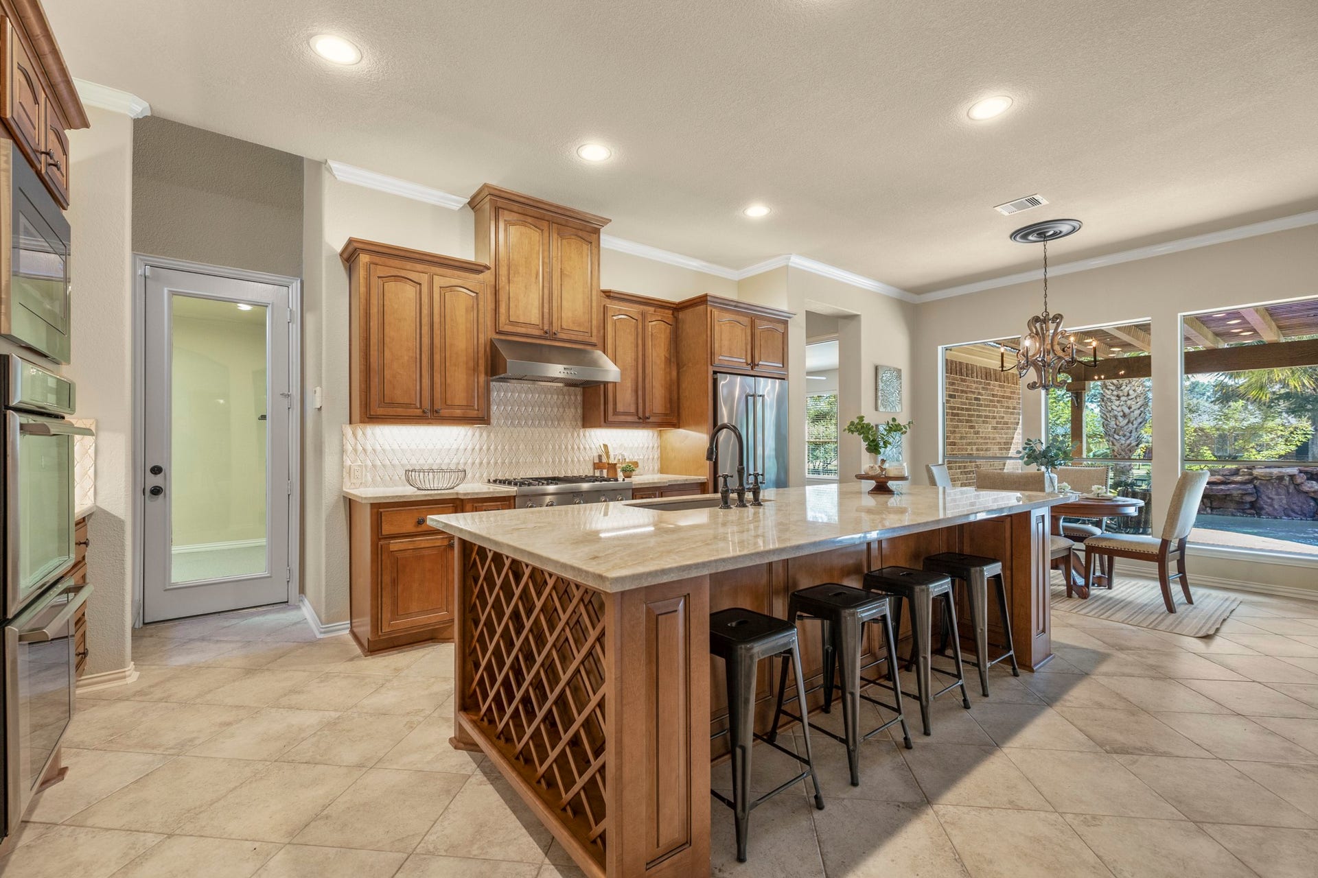 2407 Hendricks Lakes Drive, Spring, TX 77388 Inside the kitchen, the homes custom finish really comes together with Taj Mahal quartzite, Benedettini cabinetry, a Dal Tile backsplash, undercabinet lighting, and island seating that keeps the space warm and connected. Built-in wine storage adds a thoughtful detail at the end of the island, while the glass door on the left leads to the separate third garage bay and the breakfast nook ahead opens the view toward the covered patio, pool, and water-front backdrop beyond.