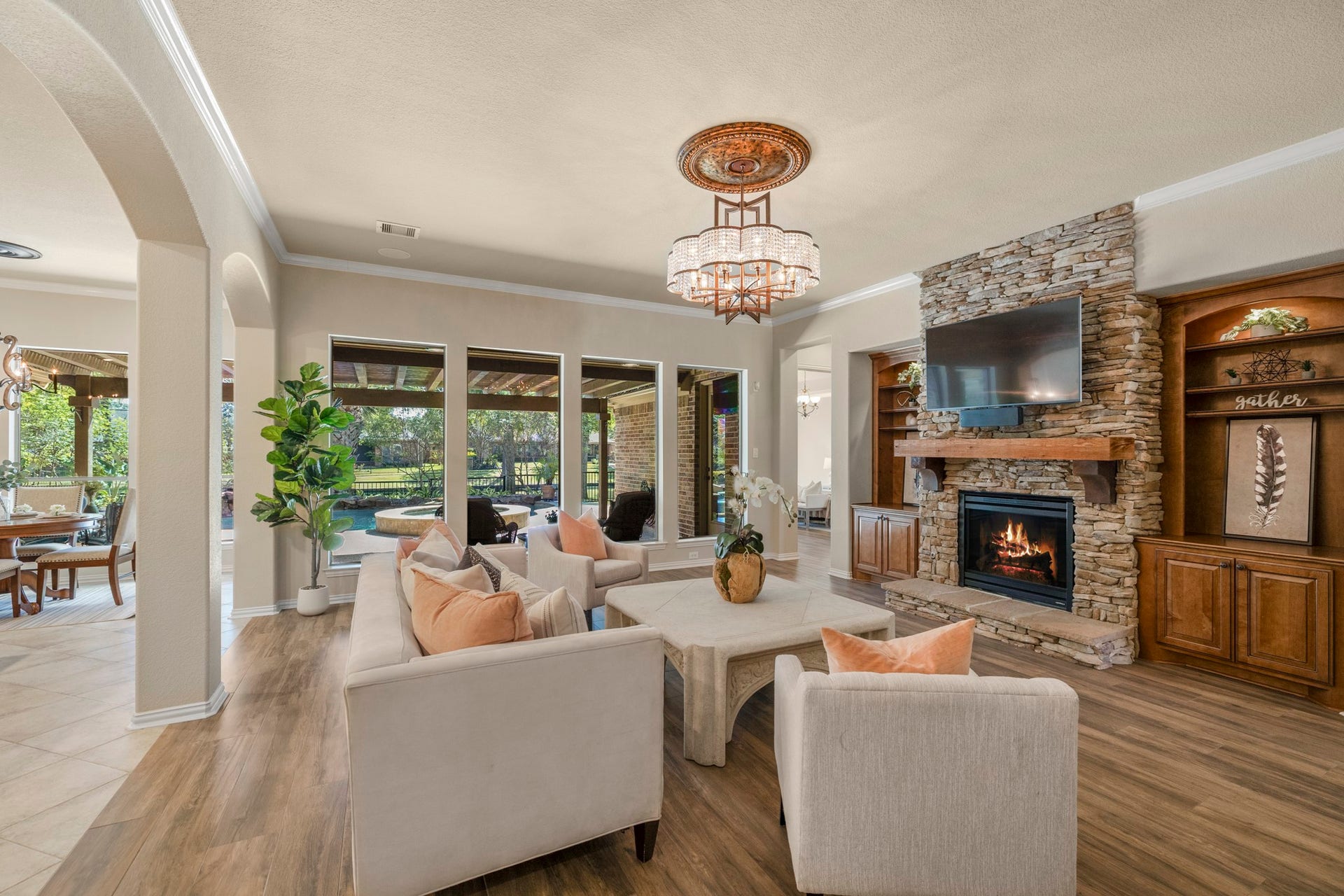 2407 Hendricks Lakes Drive, Spring, TX 77388 From the living room, the homes indoor-outdoor lifestyle really comes through, with rear windows framing the covered pergola, pool/spa, and water-view backyard beyond. The stone fireplace and custom lighted built-ins create a warm focal point inside, while the doorway just to the right of the fireplace leads into the primary suite, guiding the walkthrough from the main gathering space into the homes private retreat.