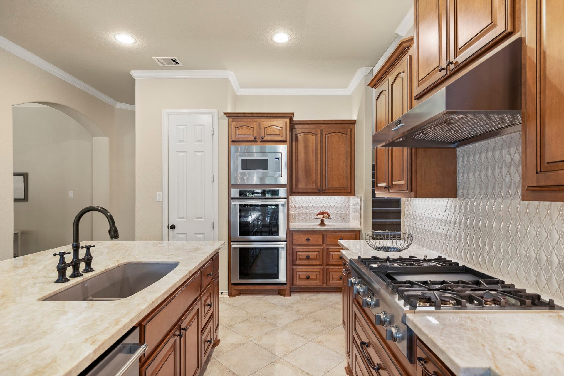 2407 Hendricks Lakes Drive, Spring, TX 77388 Along the working side of the kitchen, Taj Mahal quartzite, rich cabinetry, stainless appliances, and the upgraded tile backsplash keep the custom finish consistent from every angle. The refrigerator lines the right side, while the door on the left opens to the pantry, keeping storage close to the prep and cooking areas without interrupting the flow back toward the island.