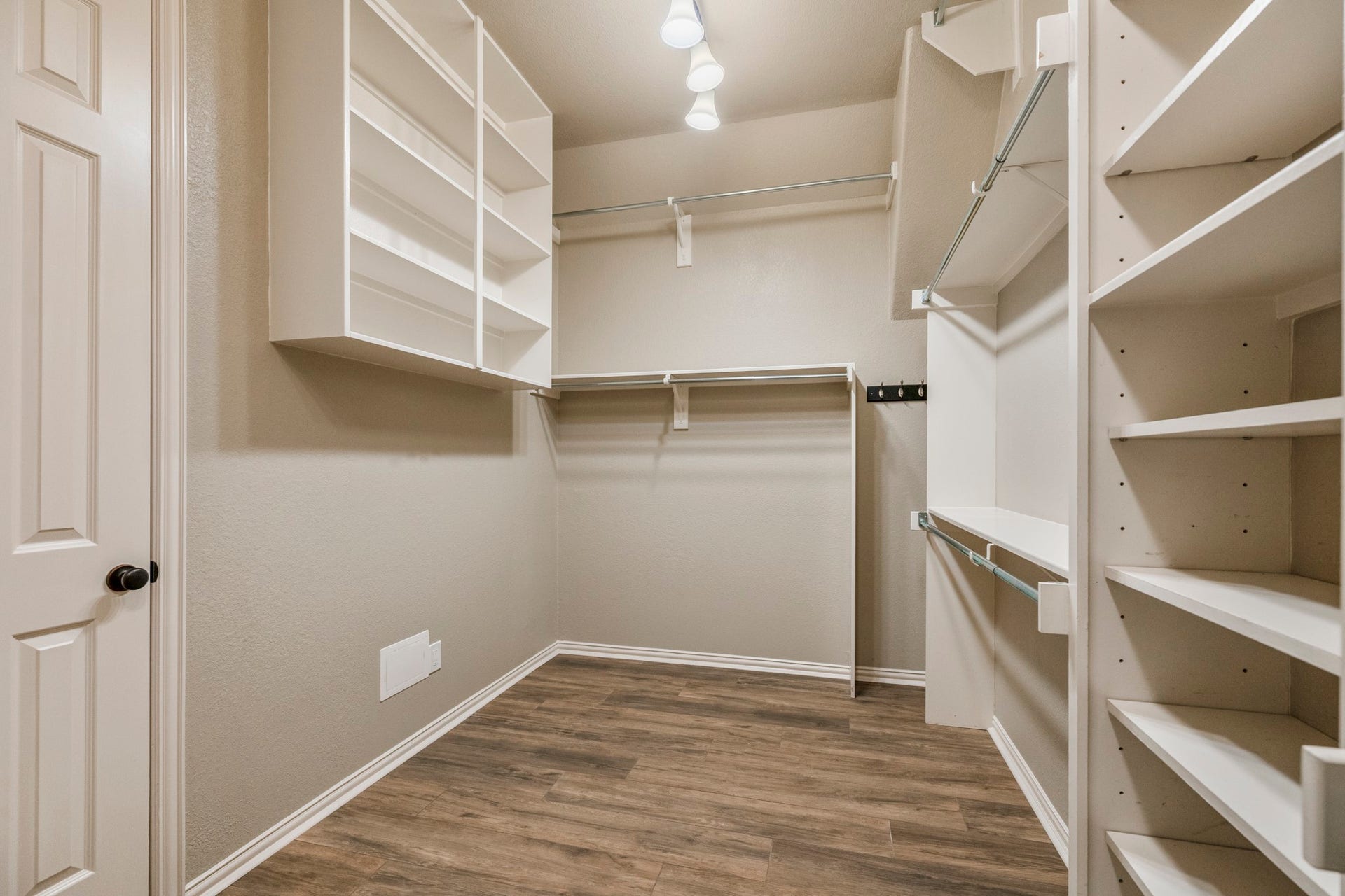 2407 Hendricks Lakes Drive, Spring, TX 77388 Another view of the primary walk-in closet shows the storage continuing with built-in shelving, hanging space, and wide-plank wood-look tile carried through from the suite. The doorway on the left leads back toward the remodeled primary bath, keeping the closet connected to the bath and bedroom for a smooth, private flow within the primary retreat.