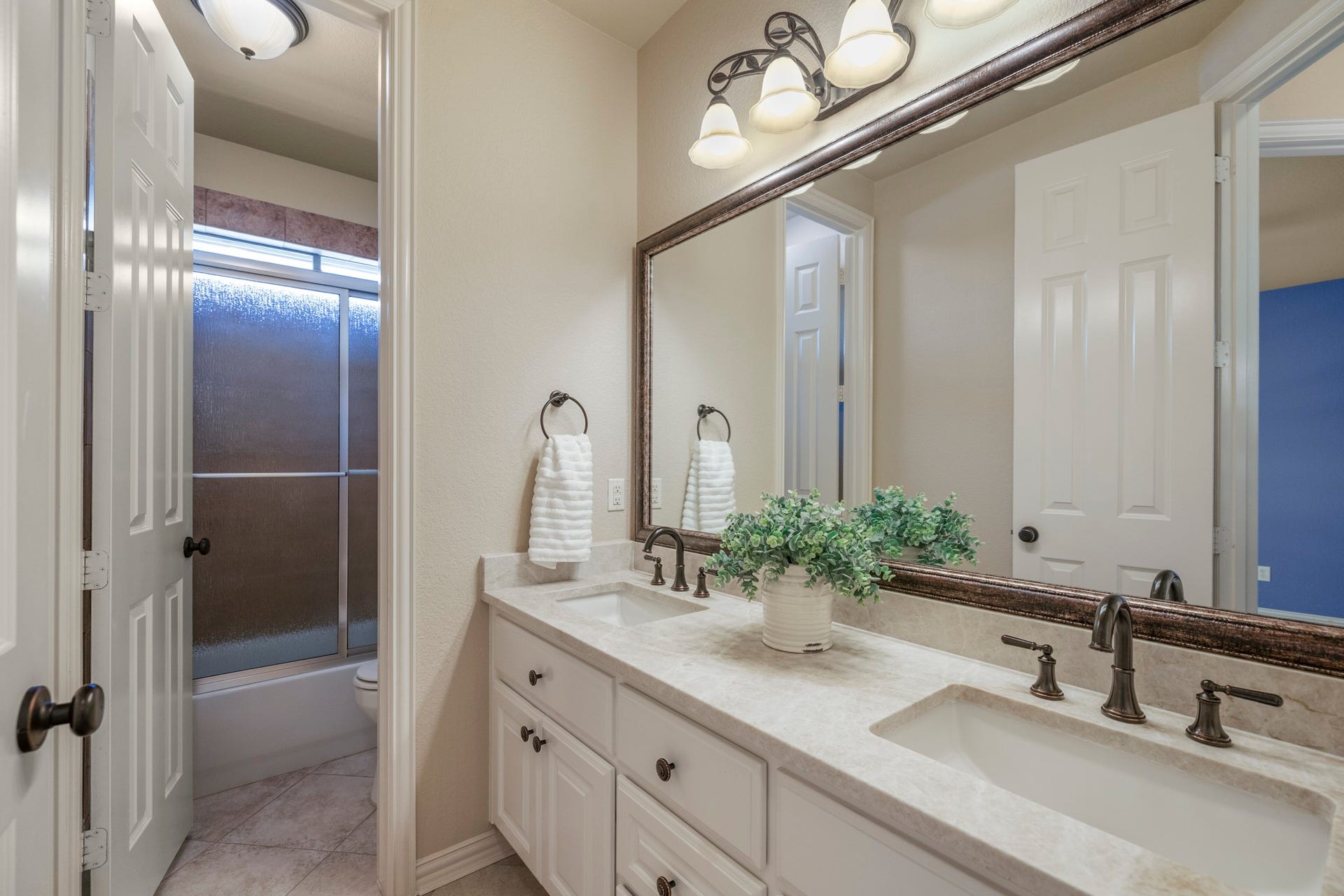 2407 Hendricks Lakes Drive, Spring, TX 77388 Connected to the second bedroom, this bath continues the suite feel with a double vanity, framed mirrors, upgraded lighting, and a glass-enclosed shower. The doorway on the left leads back into the bedroom, keeping this front-of-home space private and convenient while still feeling polished and connected to the homes custom finishes.