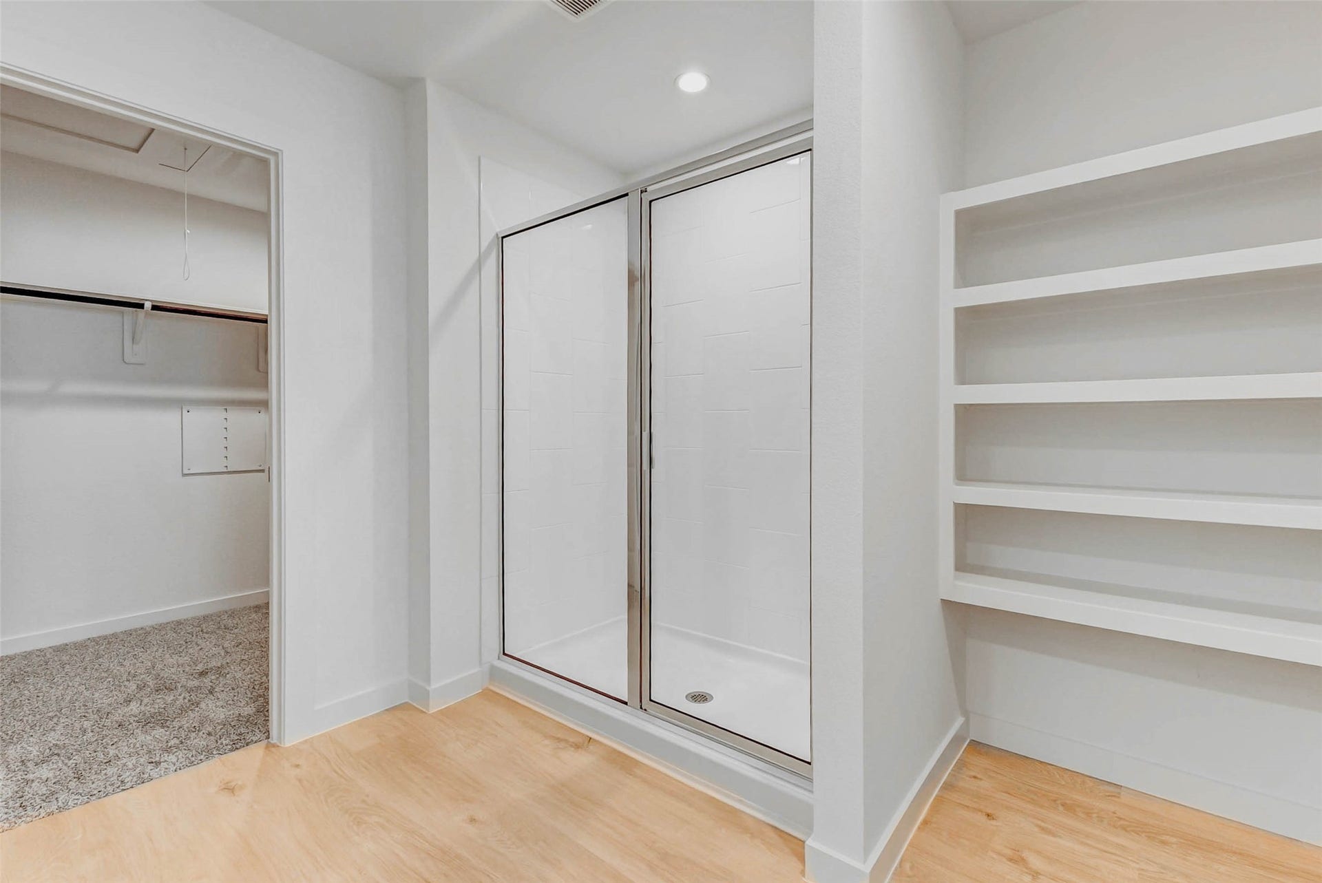 30307 Lighthouse Bluff Lane, Fulshear, TX 77441 Modern bathroom area featuring a walk-in shower with glass doors, adjacent open shelving, and a nearby carpeted walk-in closet, all with a clean, neutral palette.