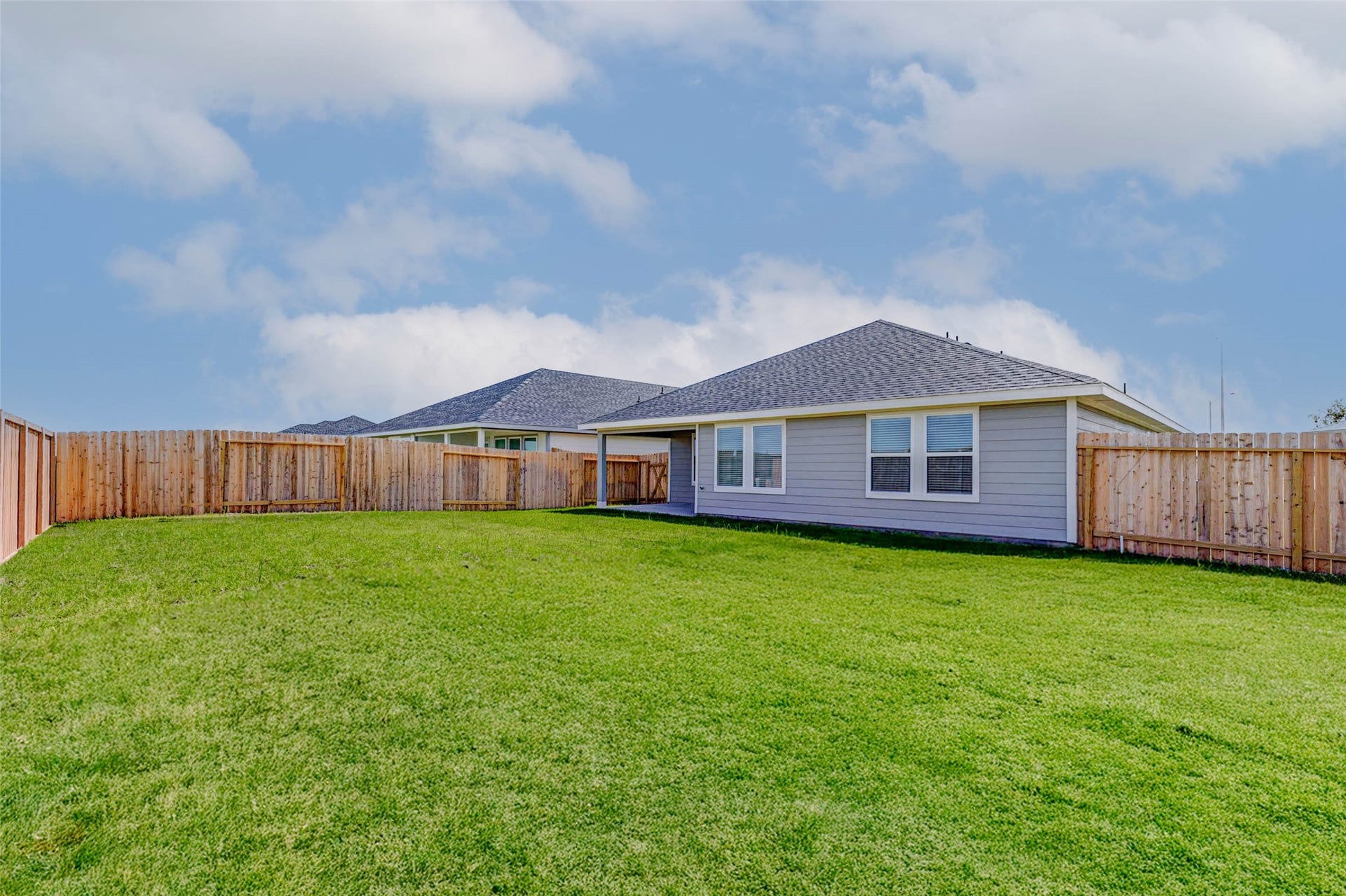 30307 Lighthouse Bluff Lane, Fulshear, TX 77441 Spacious fenced backyard with lush green lawn, perfect for outdoor activities and privacy. Modern single-story home with a light exterior and multiple windows allowing natural light.